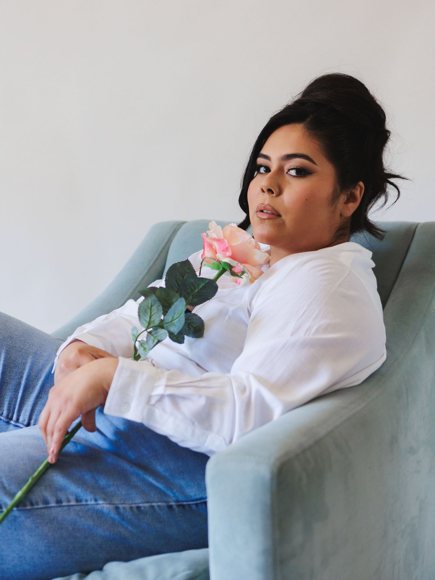 Person in white button-down and denim reclines on light blue sofa with pink roses.