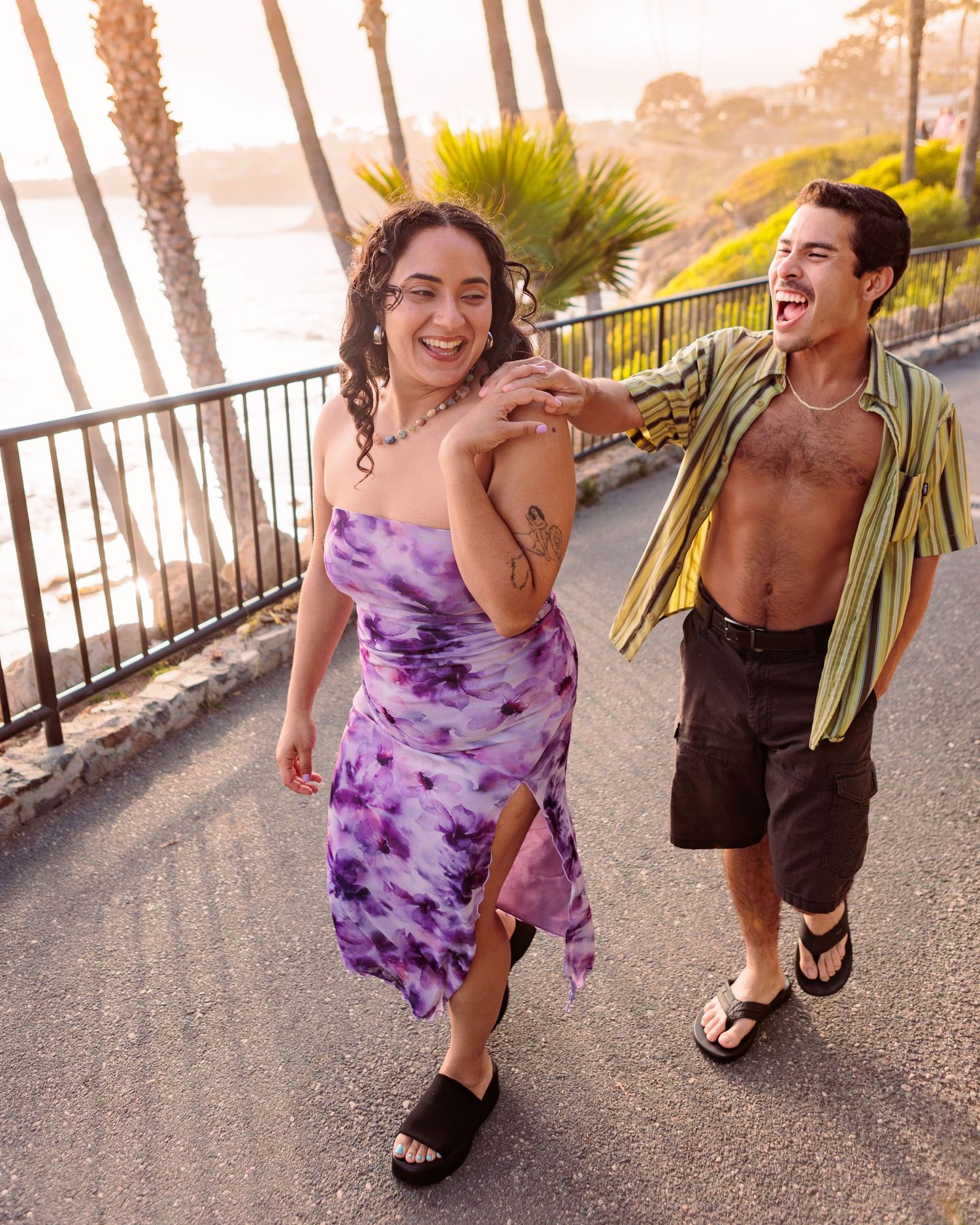 Couple in casual summer outfits enjoying a walk by palm trees.