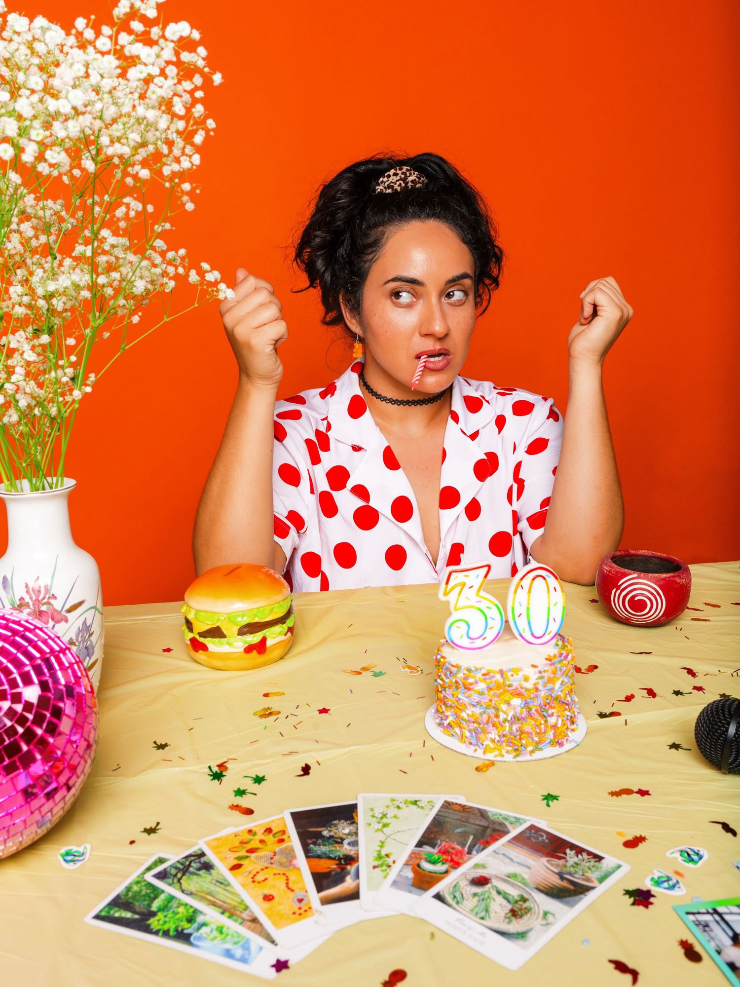 Festive table setting with birthday cake, photos, and decorations against orange background.