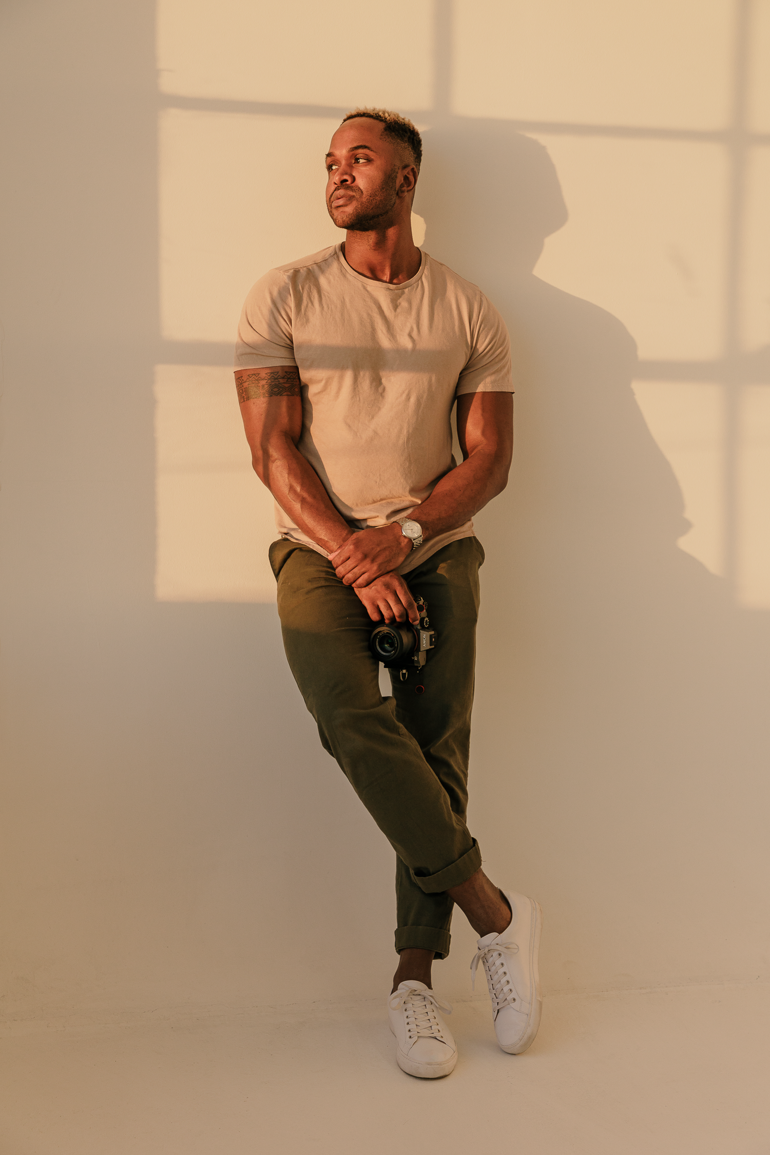 Model in white t-shirt and olive pants poses in studio with dramatic lighting and shadows.