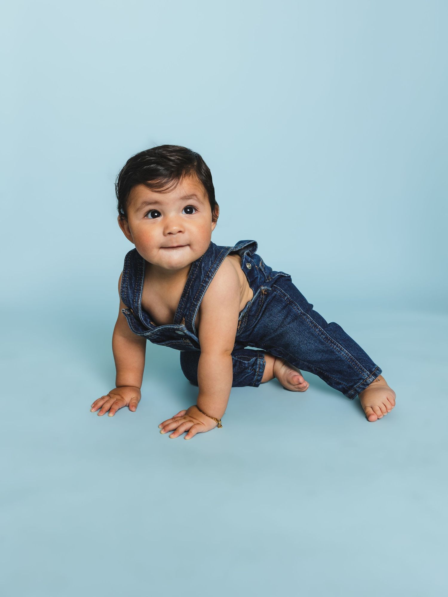 Baby in blue denim overalls crawling and exploring during a photo shoot.