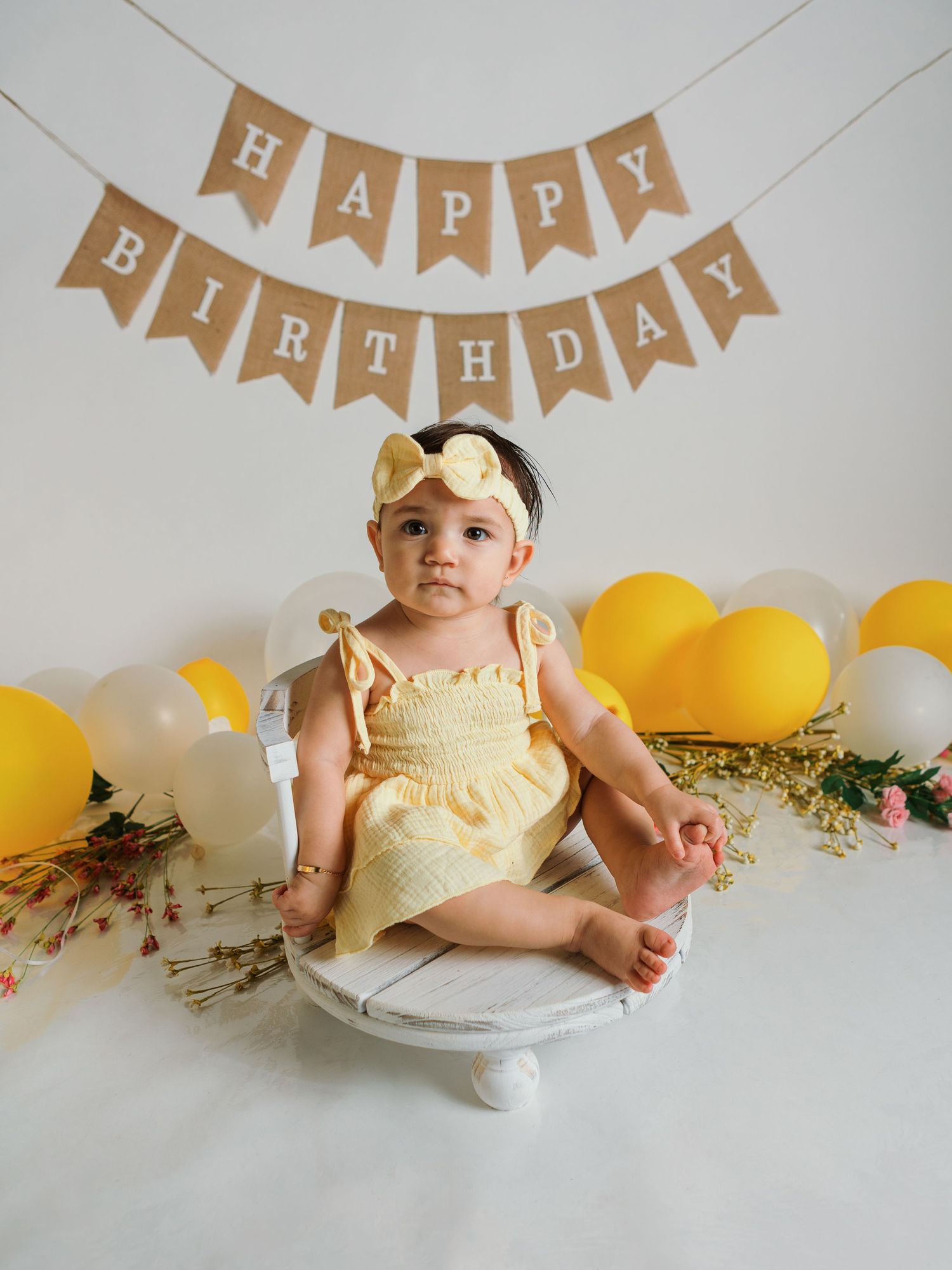 First birthday party scene with yellow dress, cake pedestal, and kraft paper banner decorations.