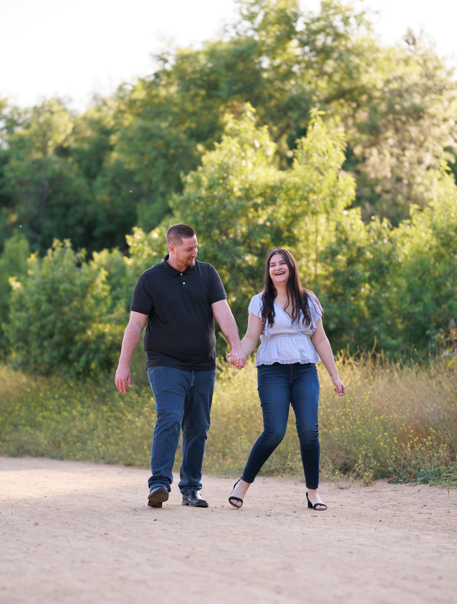 Couple walking hand in hand along a dirt path surrounded by lush greenery.