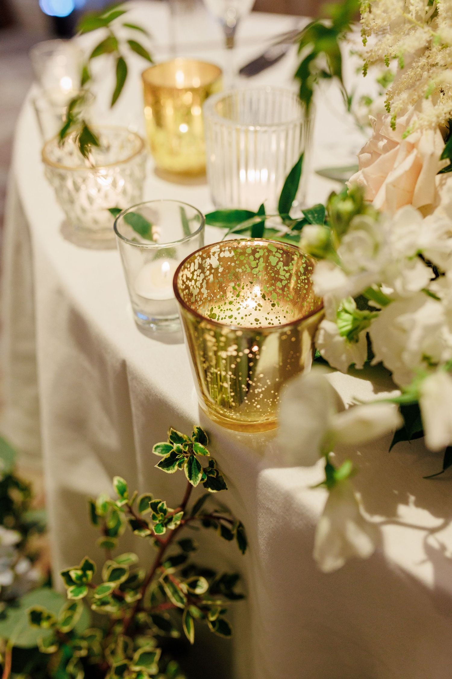 Elegant wedding reception table with gold candle holders, white flowers, and greenery decor.