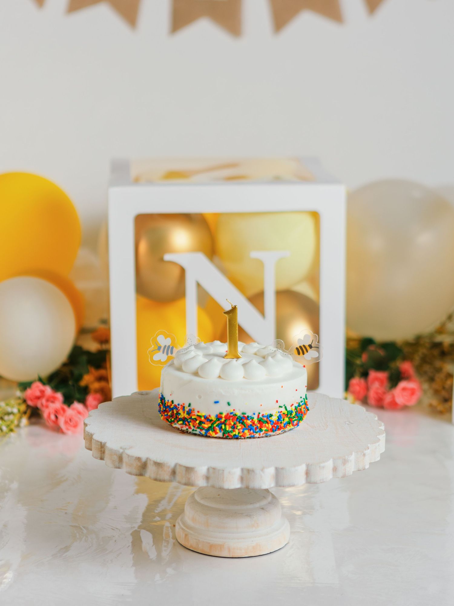 Birthday party setup with gold letters, cake stand, and yellow balloon decorations.