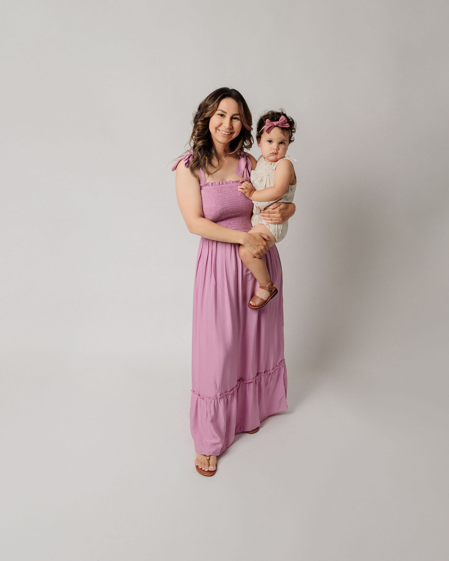 A maternity photo session against a white backdrop featuring a purple dress.