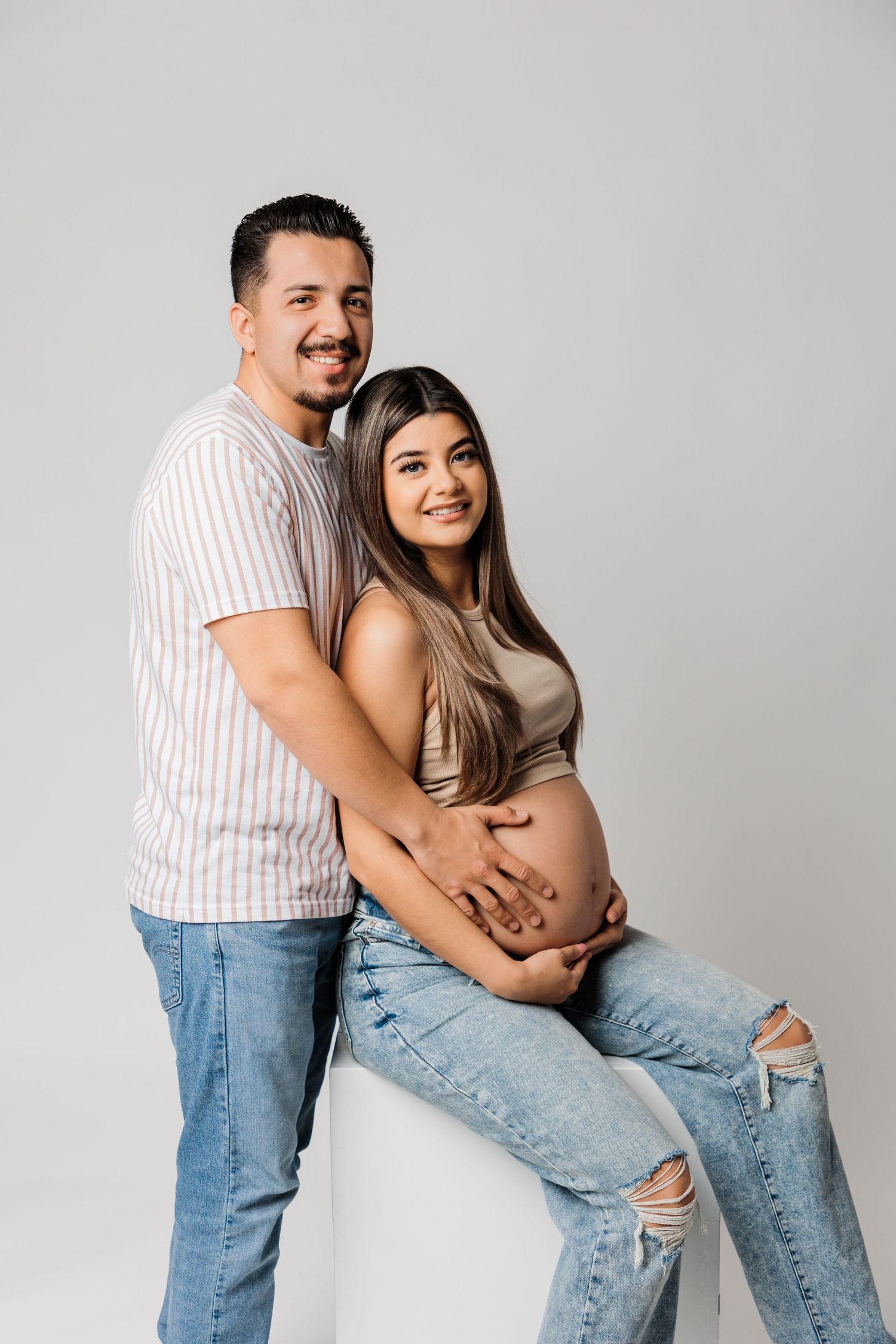 Studio maternity photos against light grey background in casual denim and stripes.