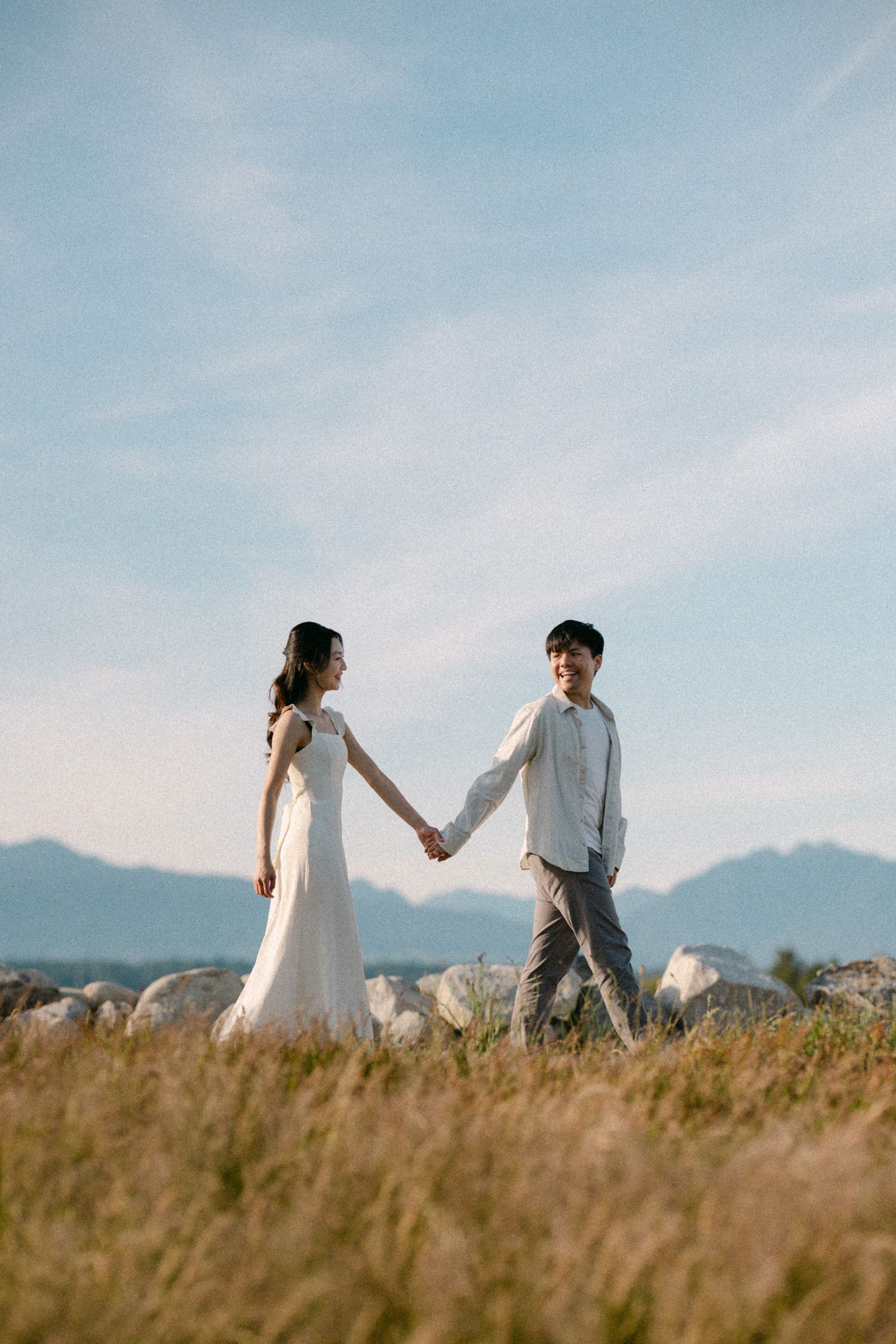 Couple walking in open fields of Terra Nova Park with mountain backdrop. Vancouver prewedding and engagement by Victor Li Photography.