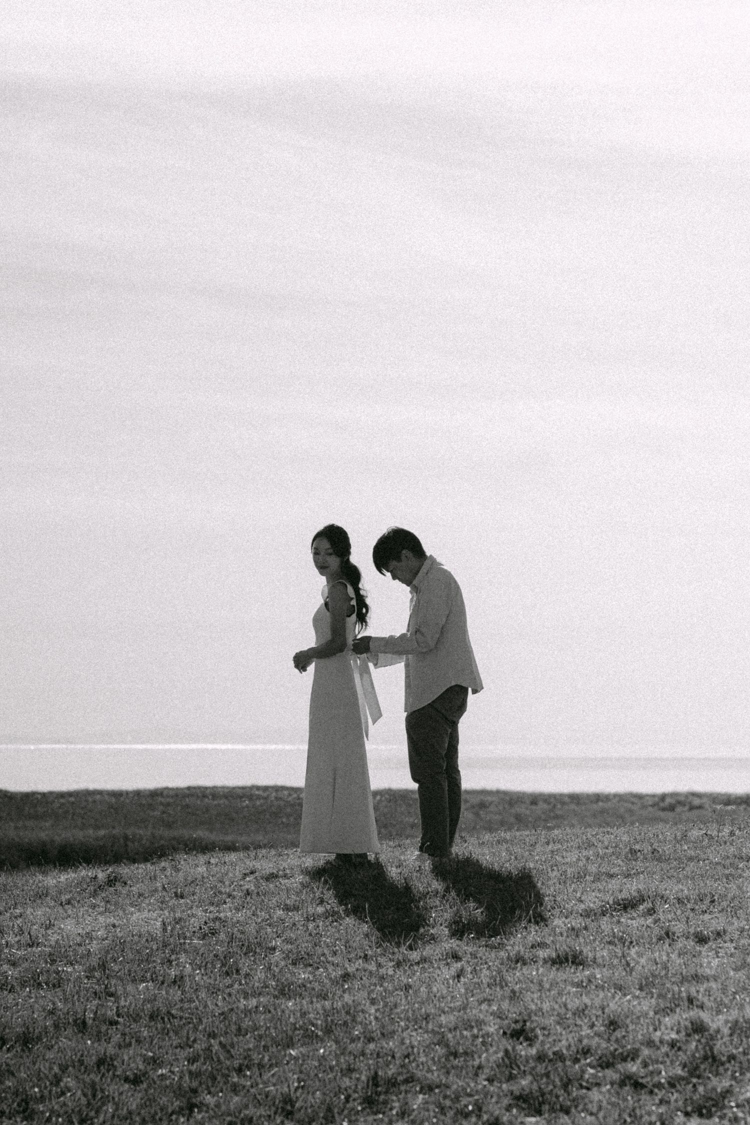 Wide shot of partner helping to tie her dress. Vancouver prewedding and engagement by Victor Li Photography.