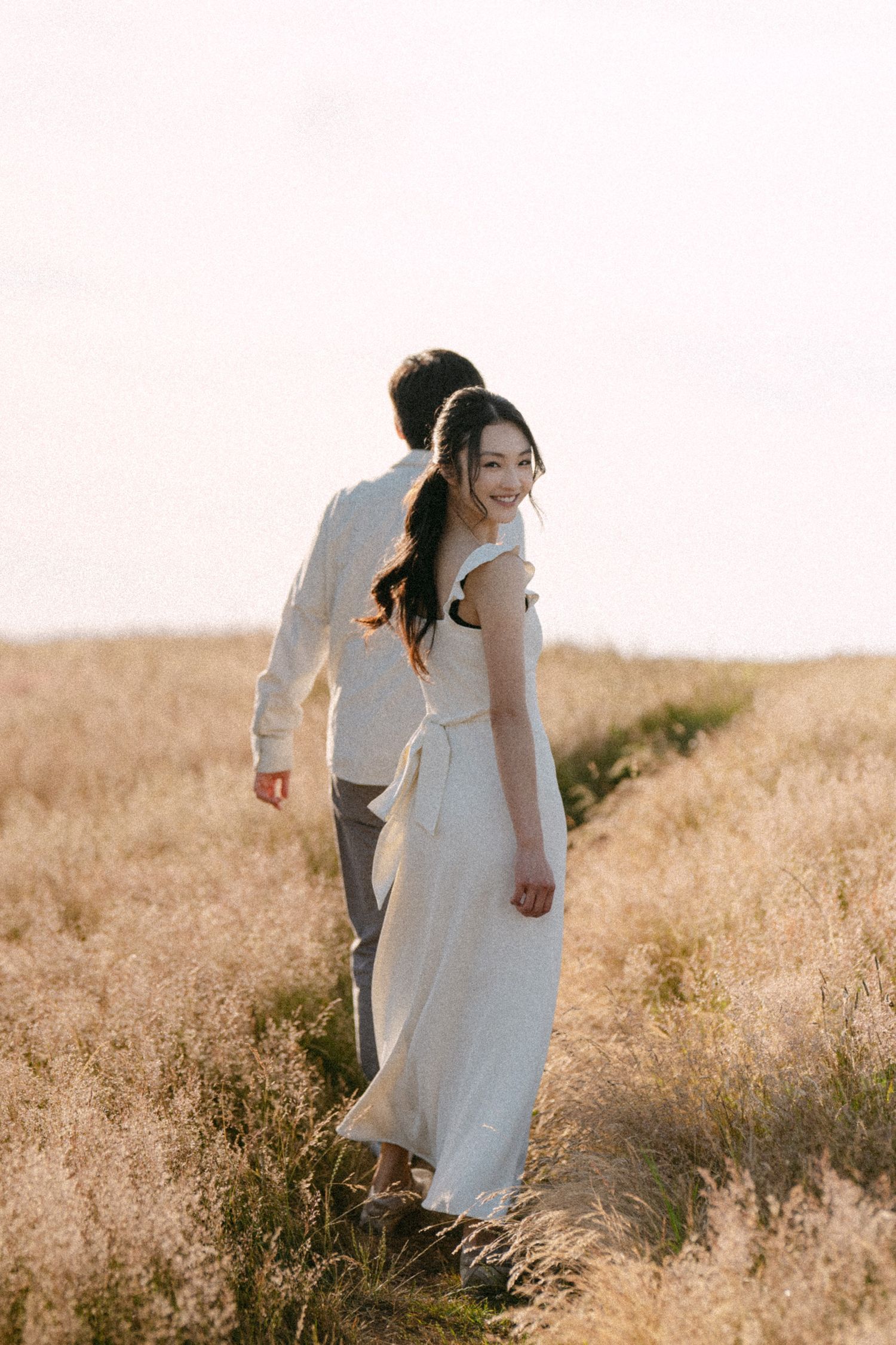 Couple walk and look back in open field at Terra Nova Park. Vancouver prewedding and engagement by Victor Li Photography.