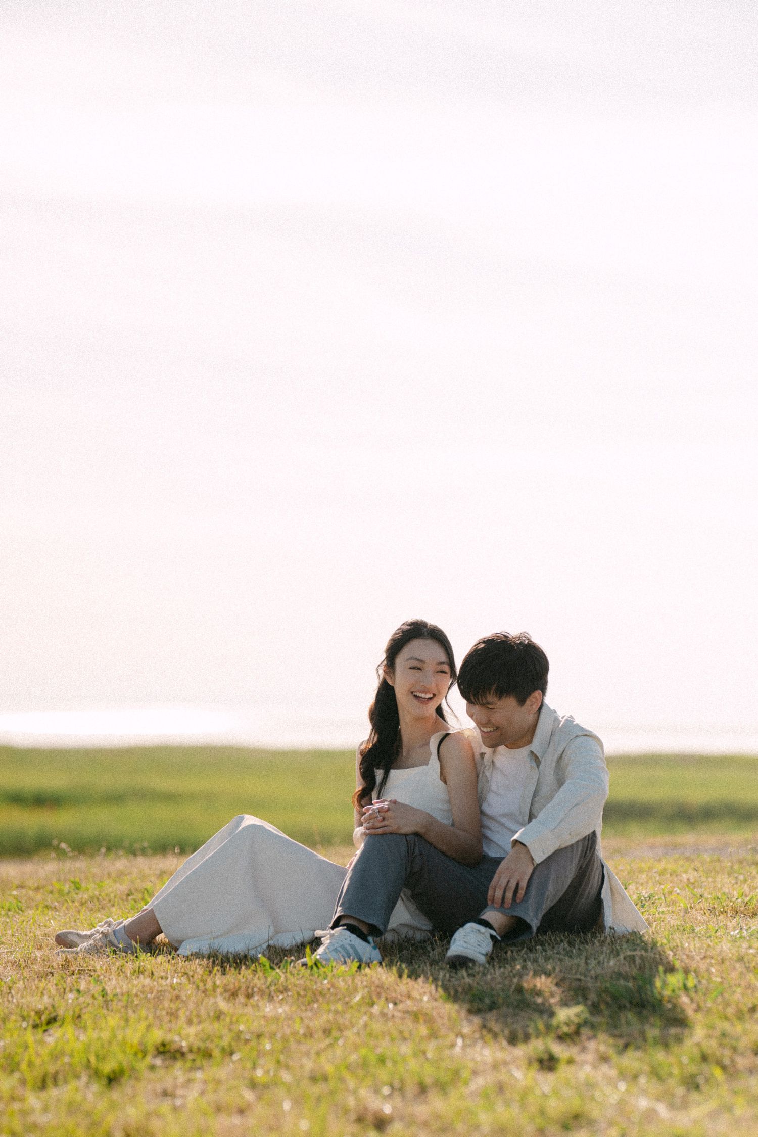 Couple sitting and laughing at Terra Nova Park. Vancouver prewedding and engagement by Victor Li Photography.