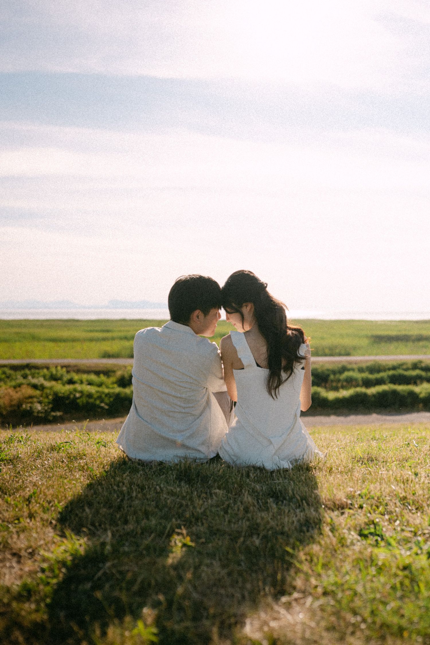 Couple sitting closely on hill at Terra Nova Park. Vancouver prewedding and engagement by Victor Li Photography.