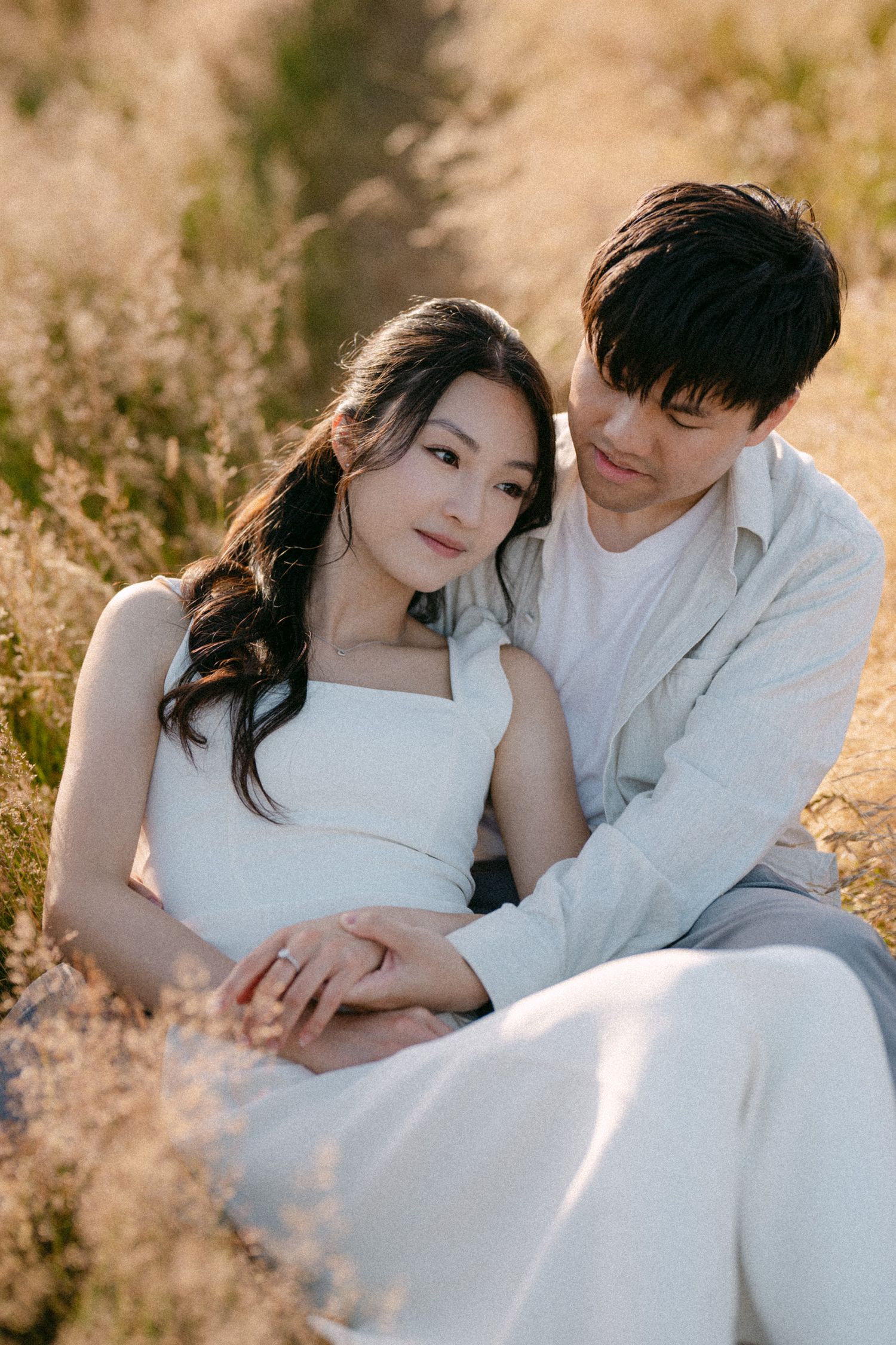 Couple sitting in open field at Terra Nova Park. Vancouver prewedding and engagement by Victor Li Photography.