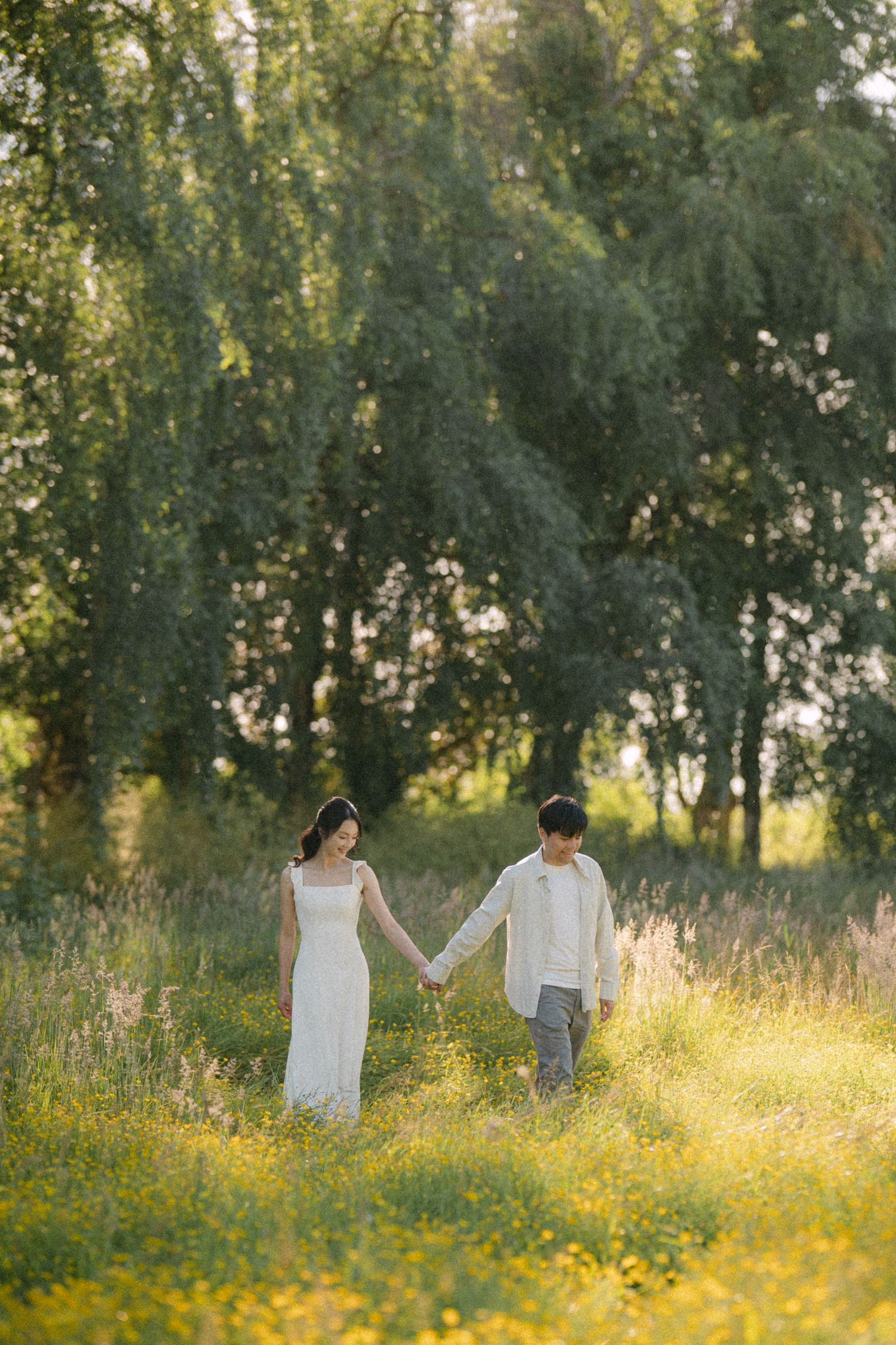 Couple walking through open field at Terra Nova Park during golden hour. Vancouver prewedding and engagement by Victor Li Photography.