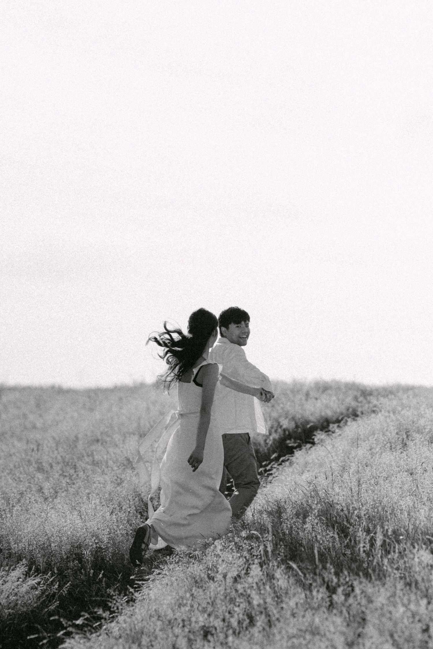 Couple running through an open field at Terra Nova Park. Vancouver prewedding and engagement by Victor Li Photography.