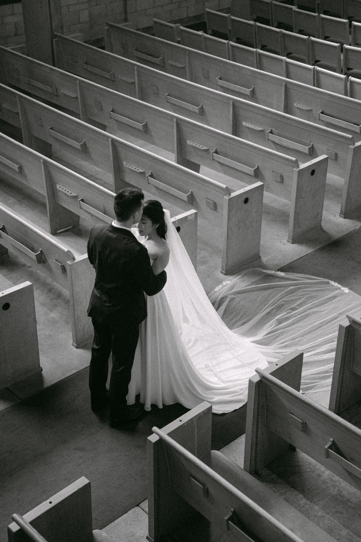Couple embraces with a kiss in church pews. Vancouver wedding by Victor Li Photography.