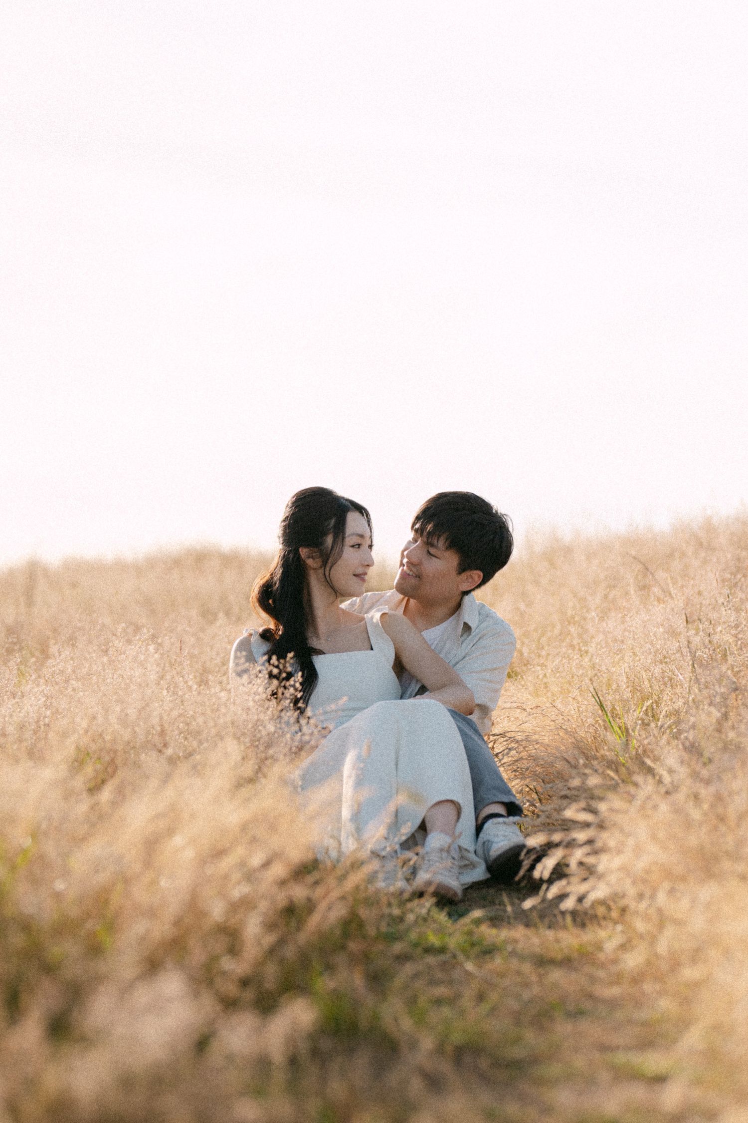 Couple sitting in open field at Terra Nova Park. Vancouver prewedding and engagement by Victor Li Photography.