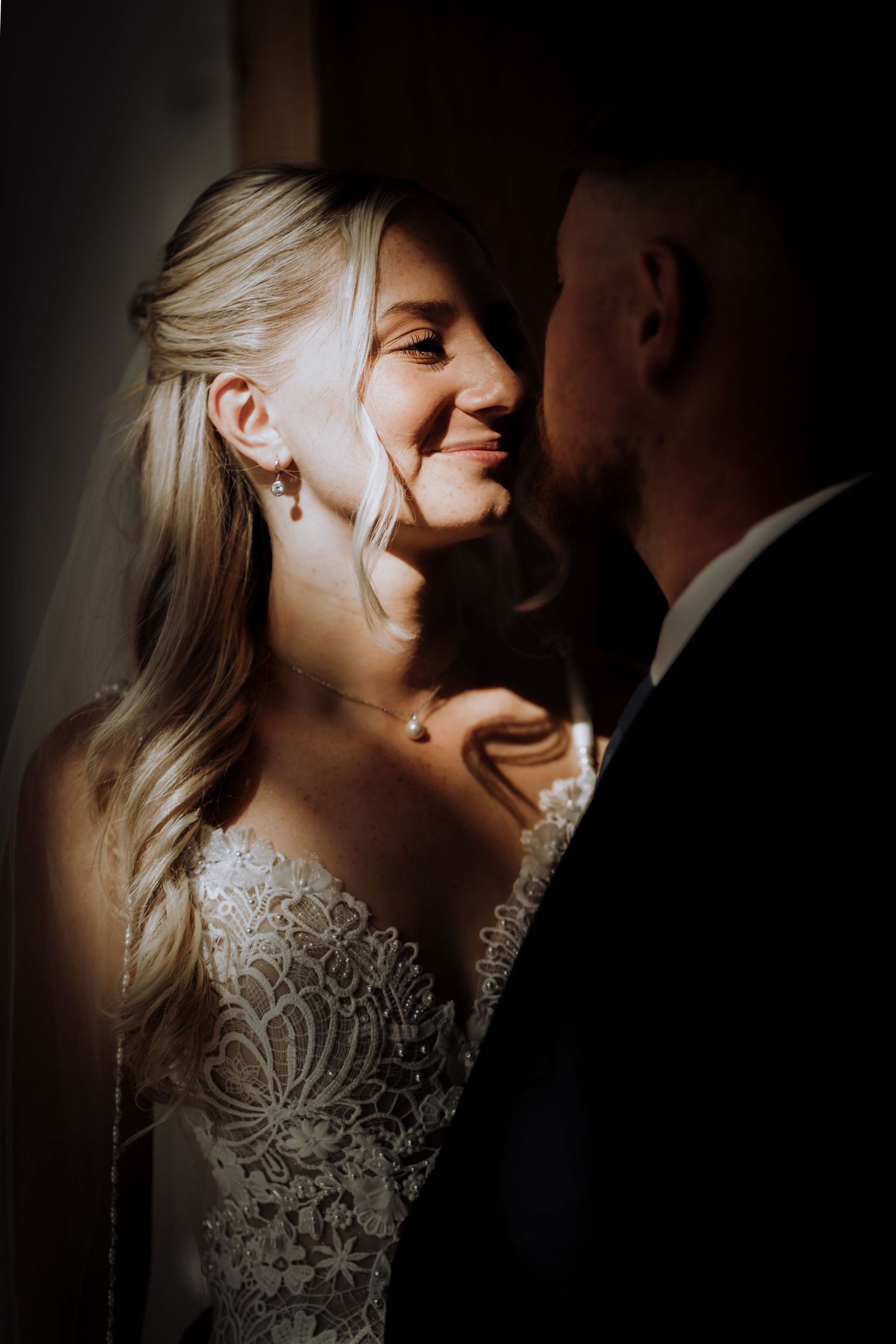 A romantic wedding couple shares an intimate moment in dramatic lighting wearing elegant bridal attire.