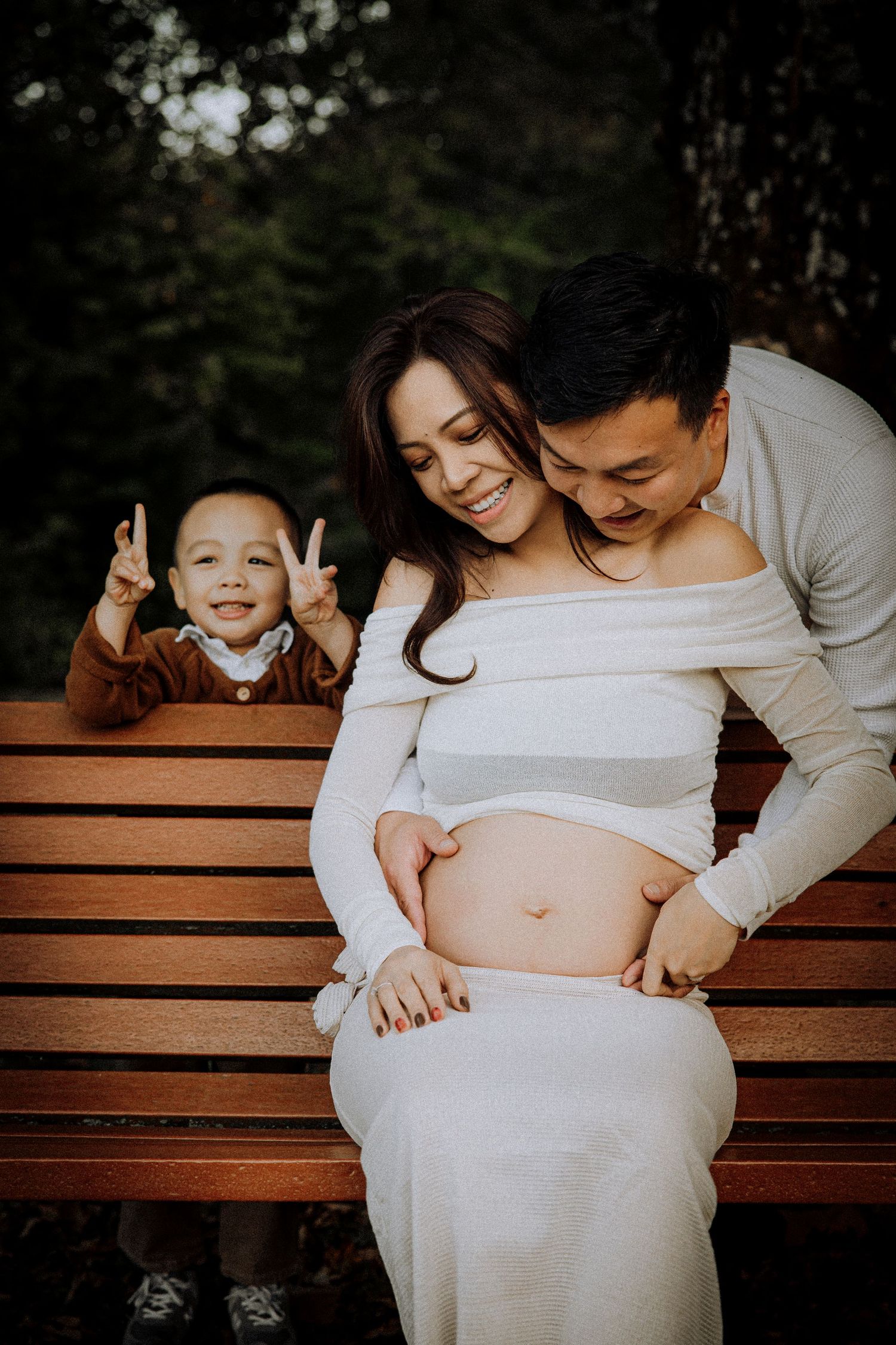Family sharing intimate moment on wooden bench during maternity photoshoot.