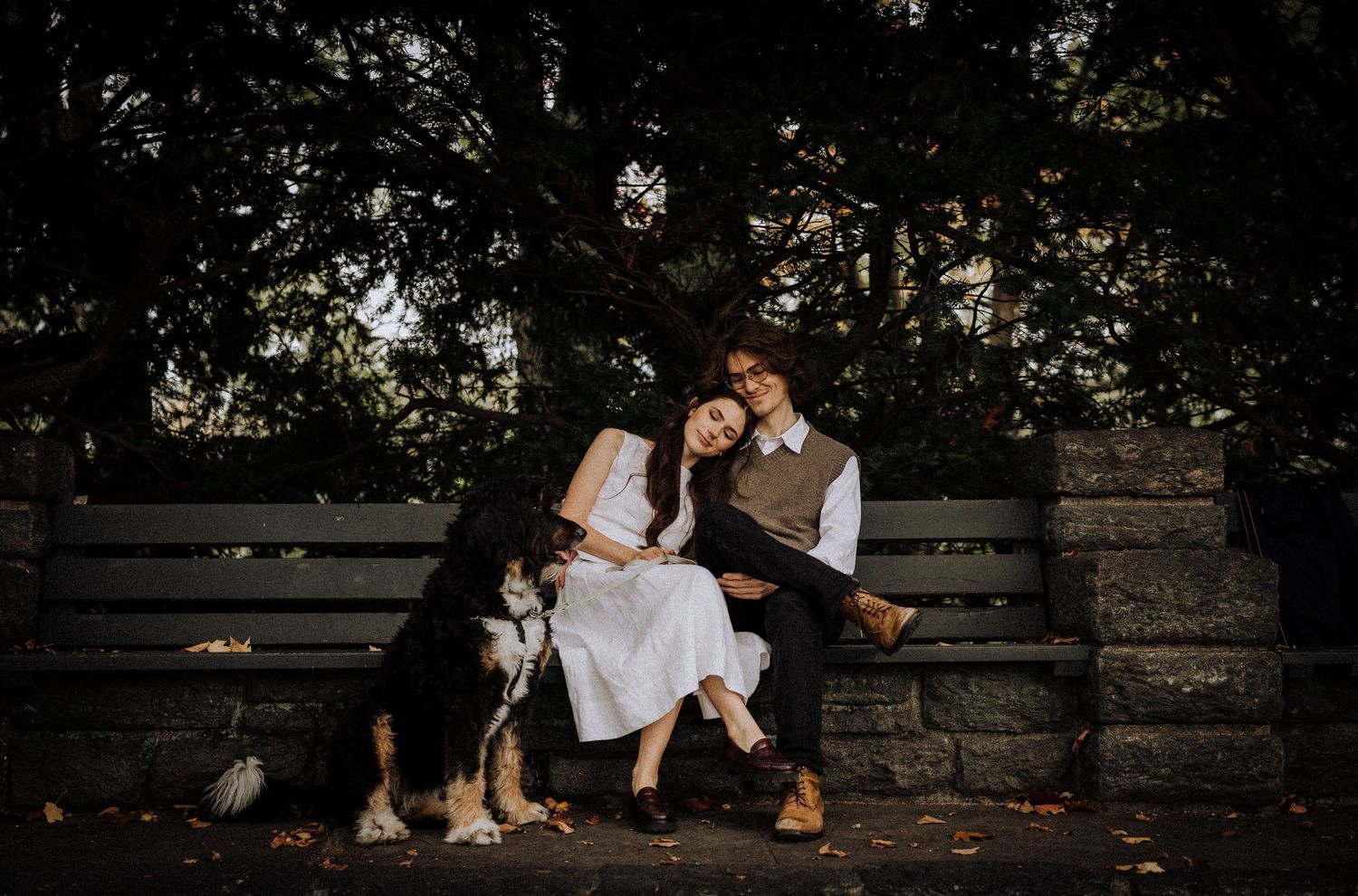 A couple shares intimate moments on a wooden bench in a park setting.