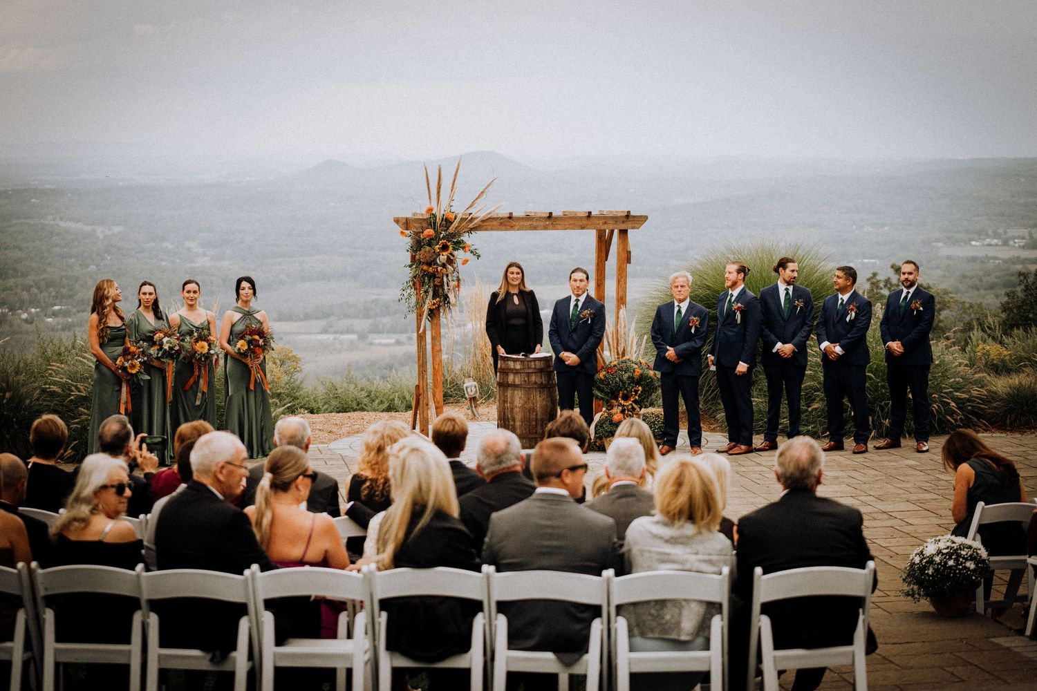 An outdoor wedding ceremony setup with wooden arch and white chairs overlooking a scenic mountain view.