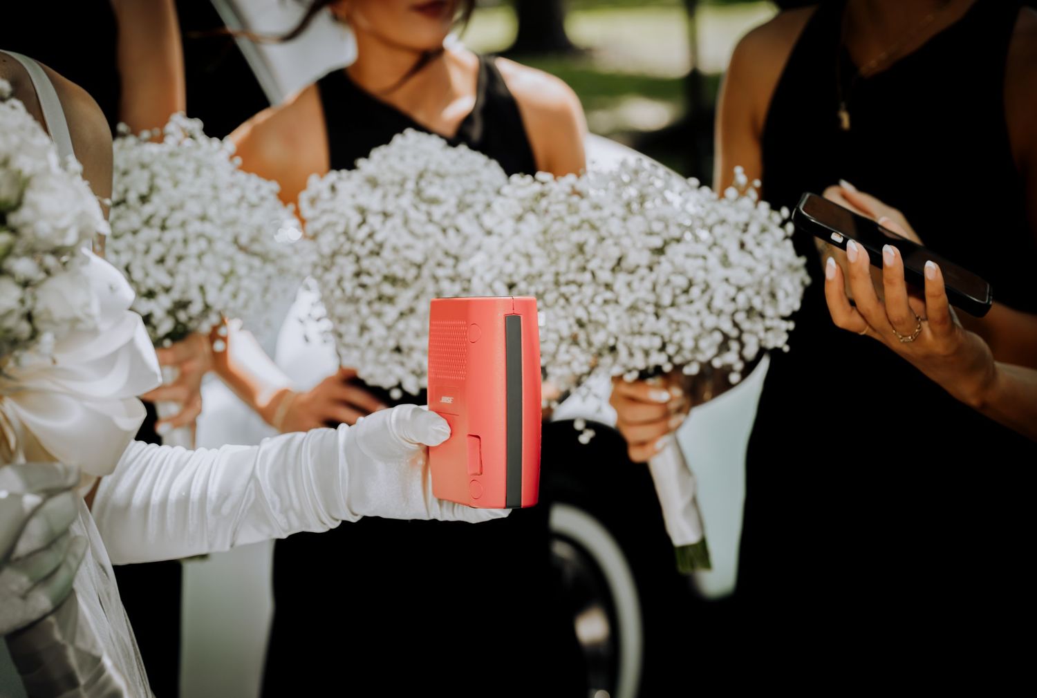 Wedding party members hold coral-colored gift boxes during an outdoor celebration.
