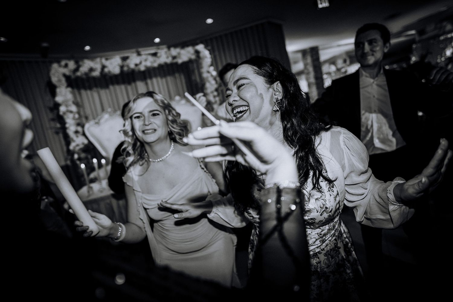 Black and white photo of guests dancing and celebrating joyfully at a lively wedding reception party.