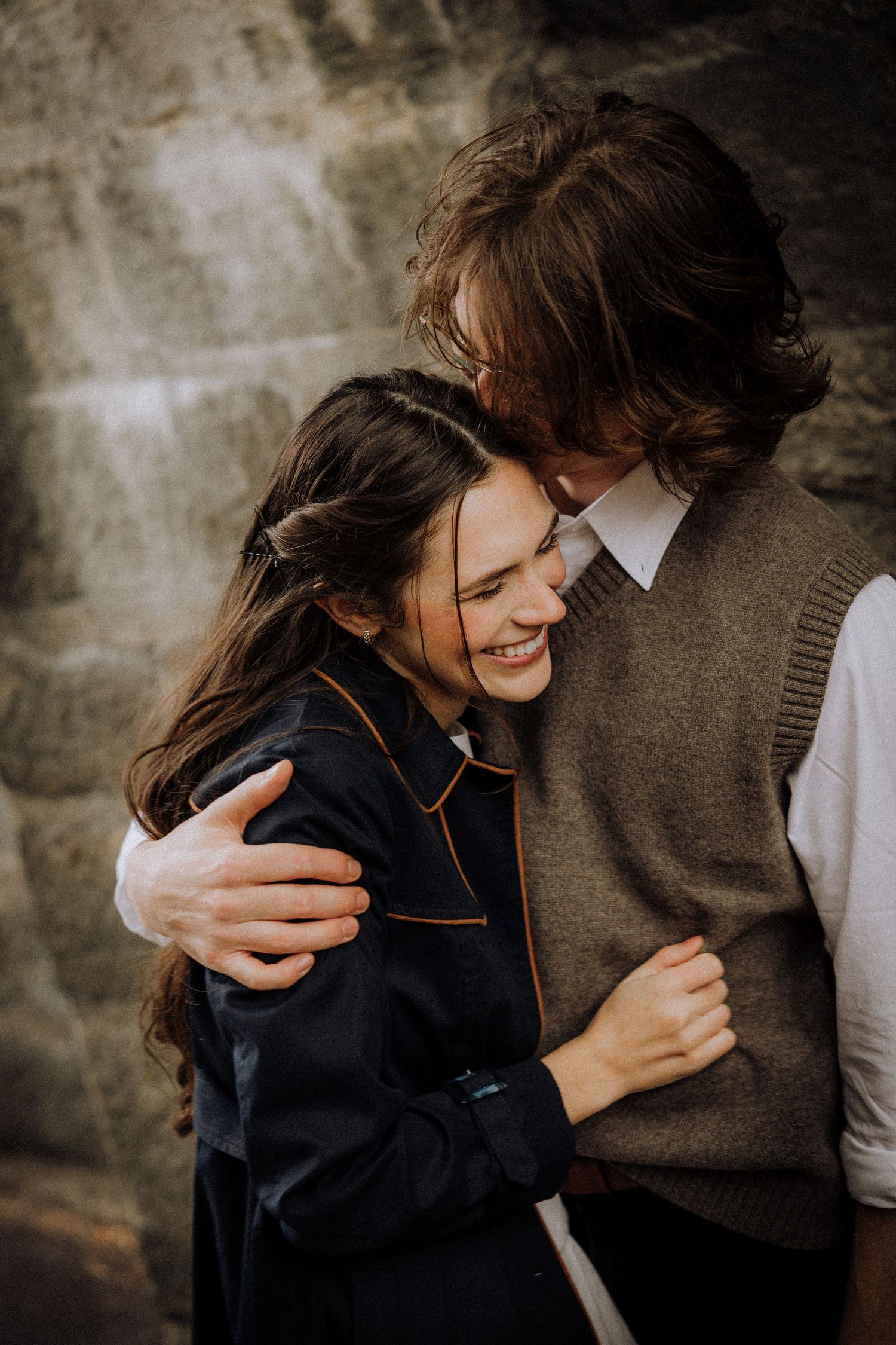 Intimate couple embraces in a series of candid romantic moments against a stone wall backdrop.