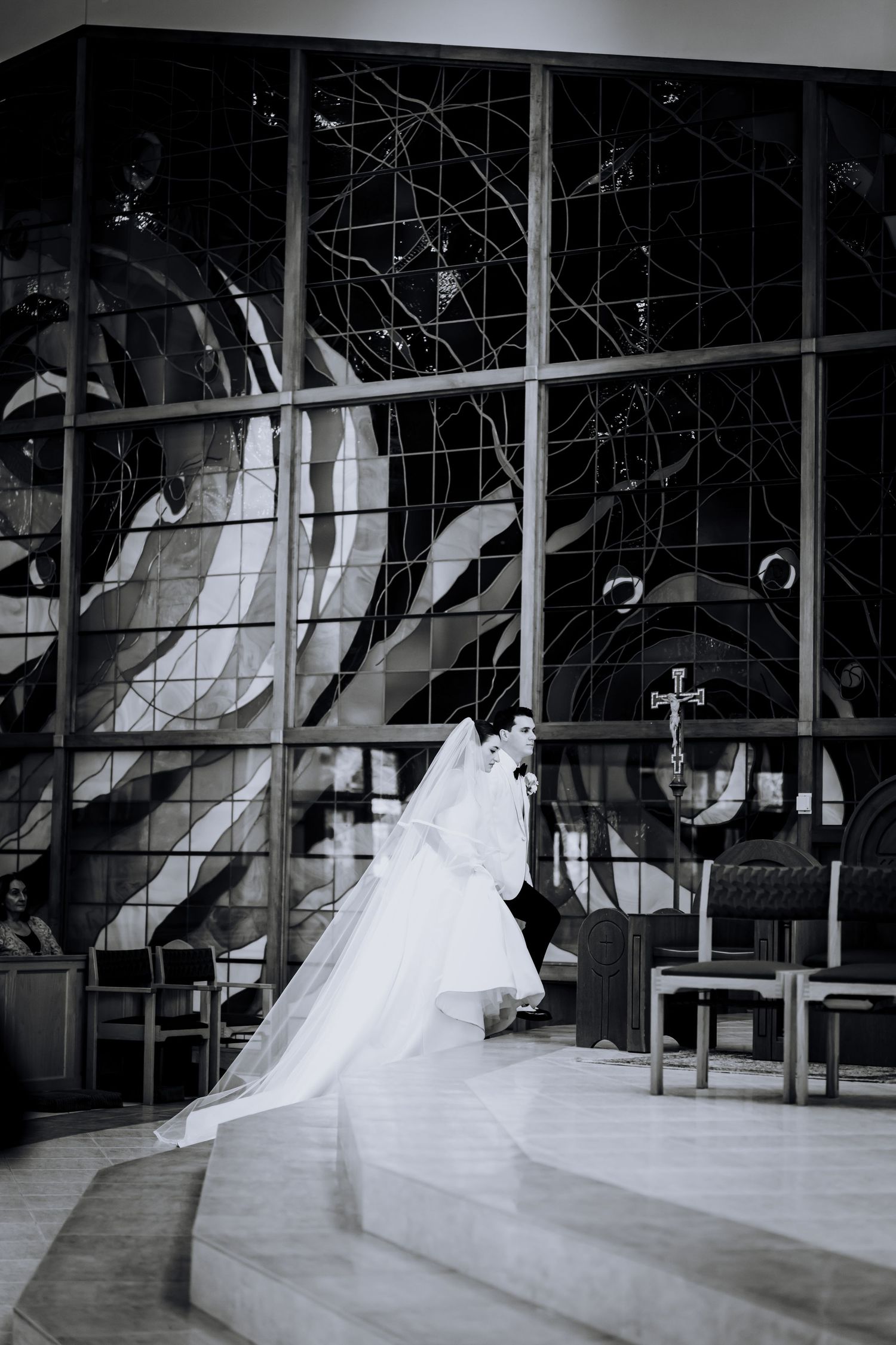 A dramatic black and white photo of a wedding dress train against geometric stained glass windows.