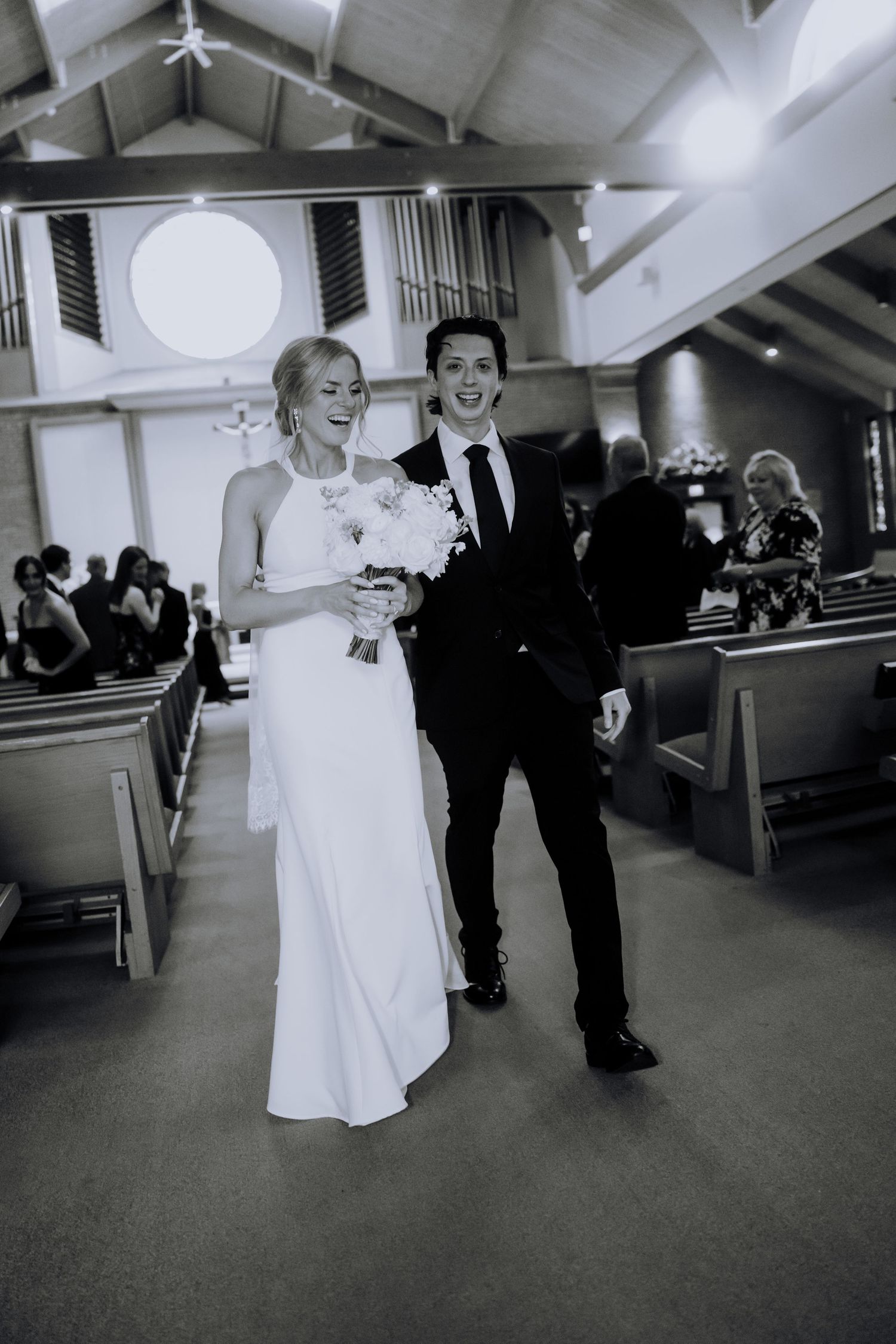 A black and white wedding photo showing a couple walking down the church aisle together after their ceremony.