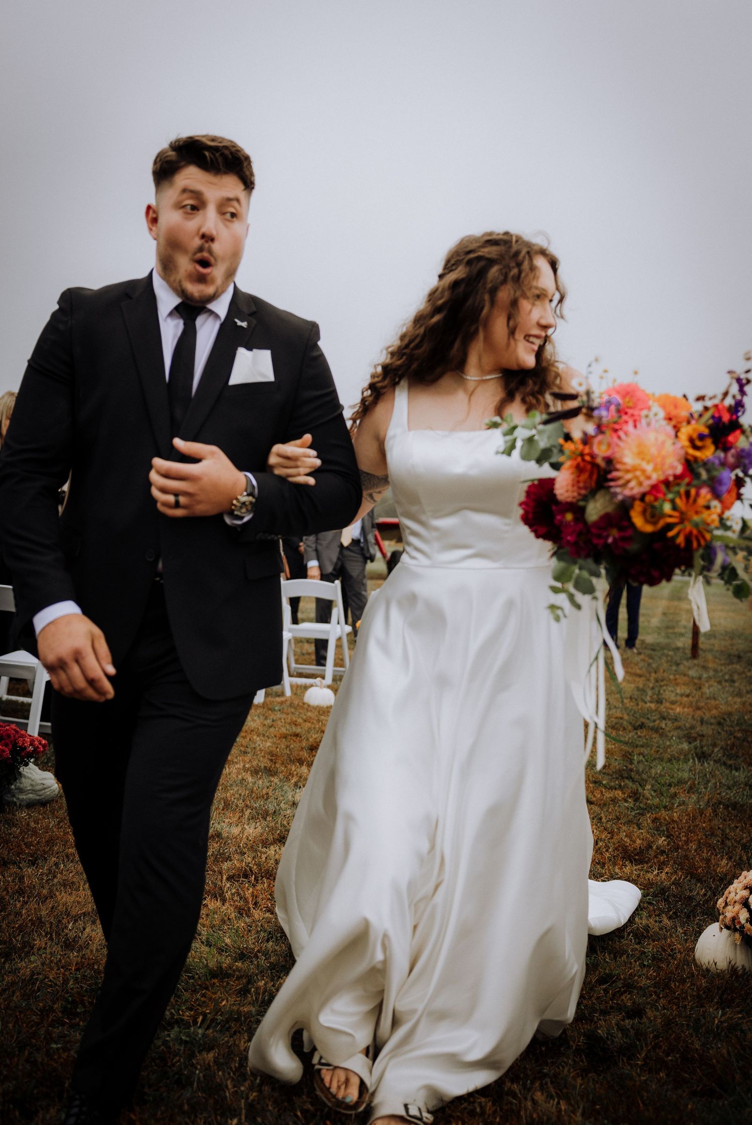A candid wedding moment shows a couple walking together outdoors with colorful fall floral arrangements.