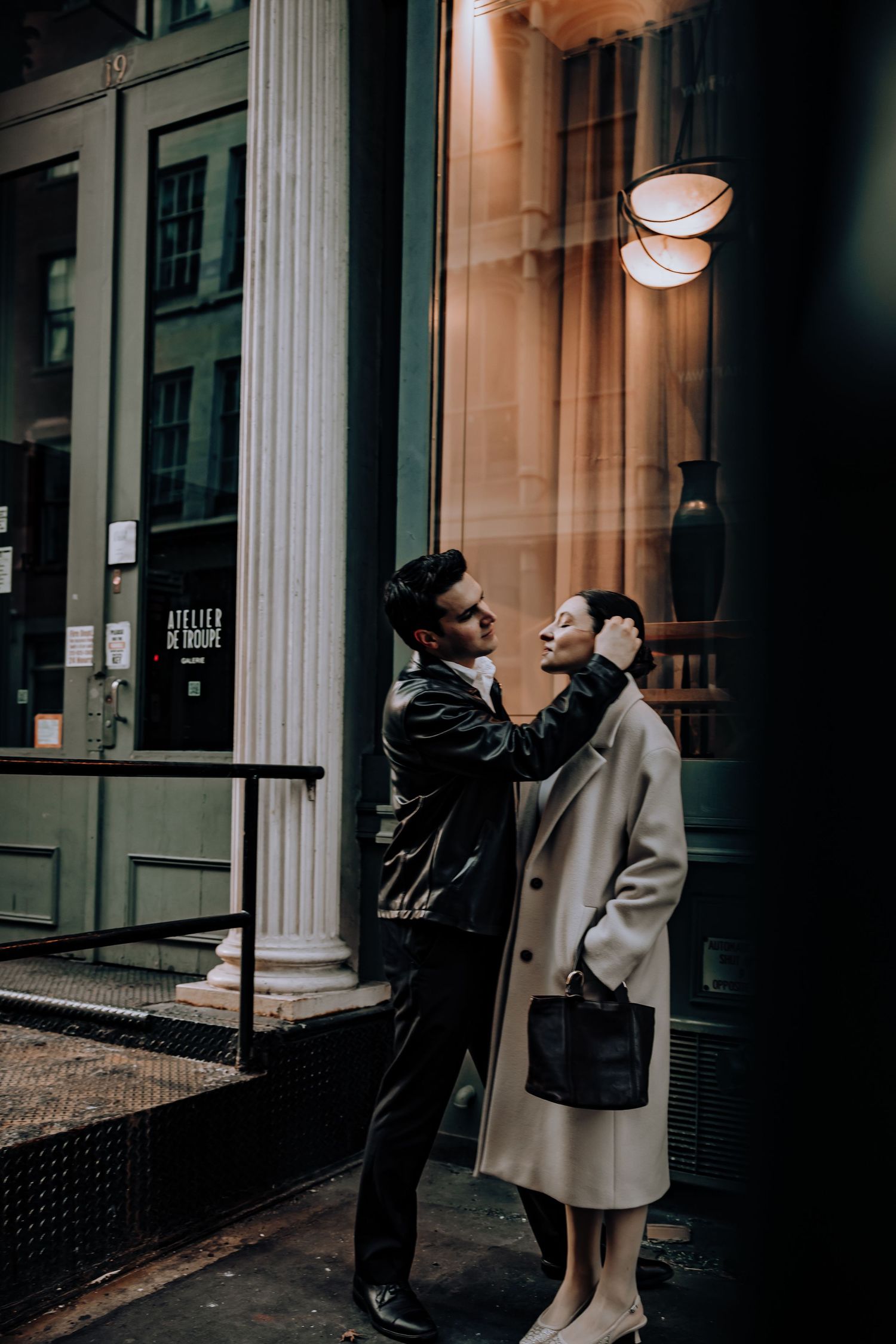 Two people pose dramatically against classical columns in moody lighting.