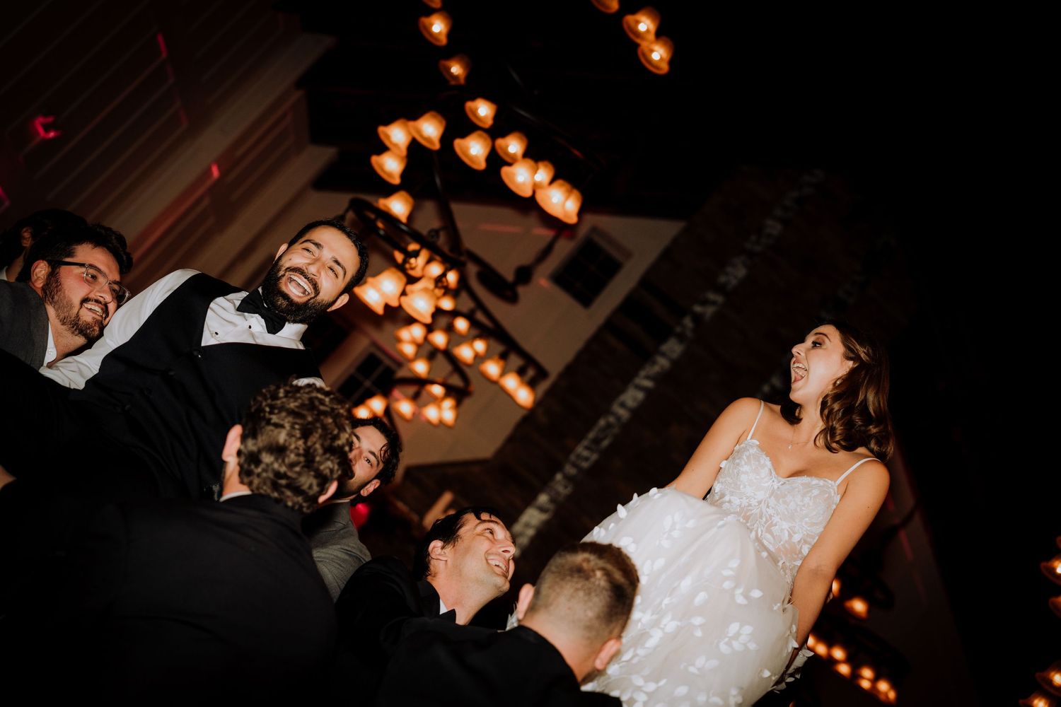 Wedding reception party scene with string lights and celebratory dancing.