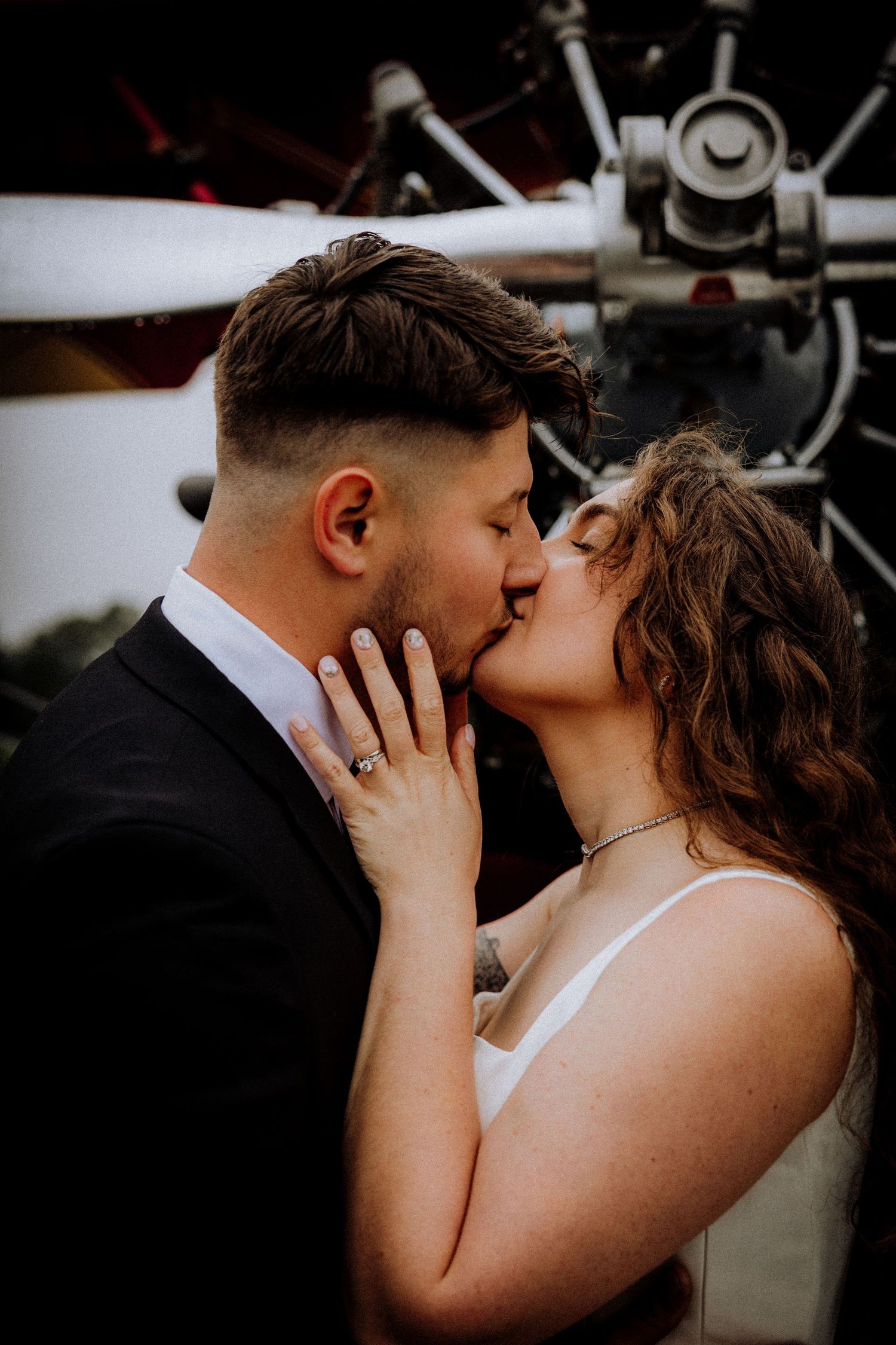 Romantic kiss between newlyweds against dark background with vintage motorcycles.