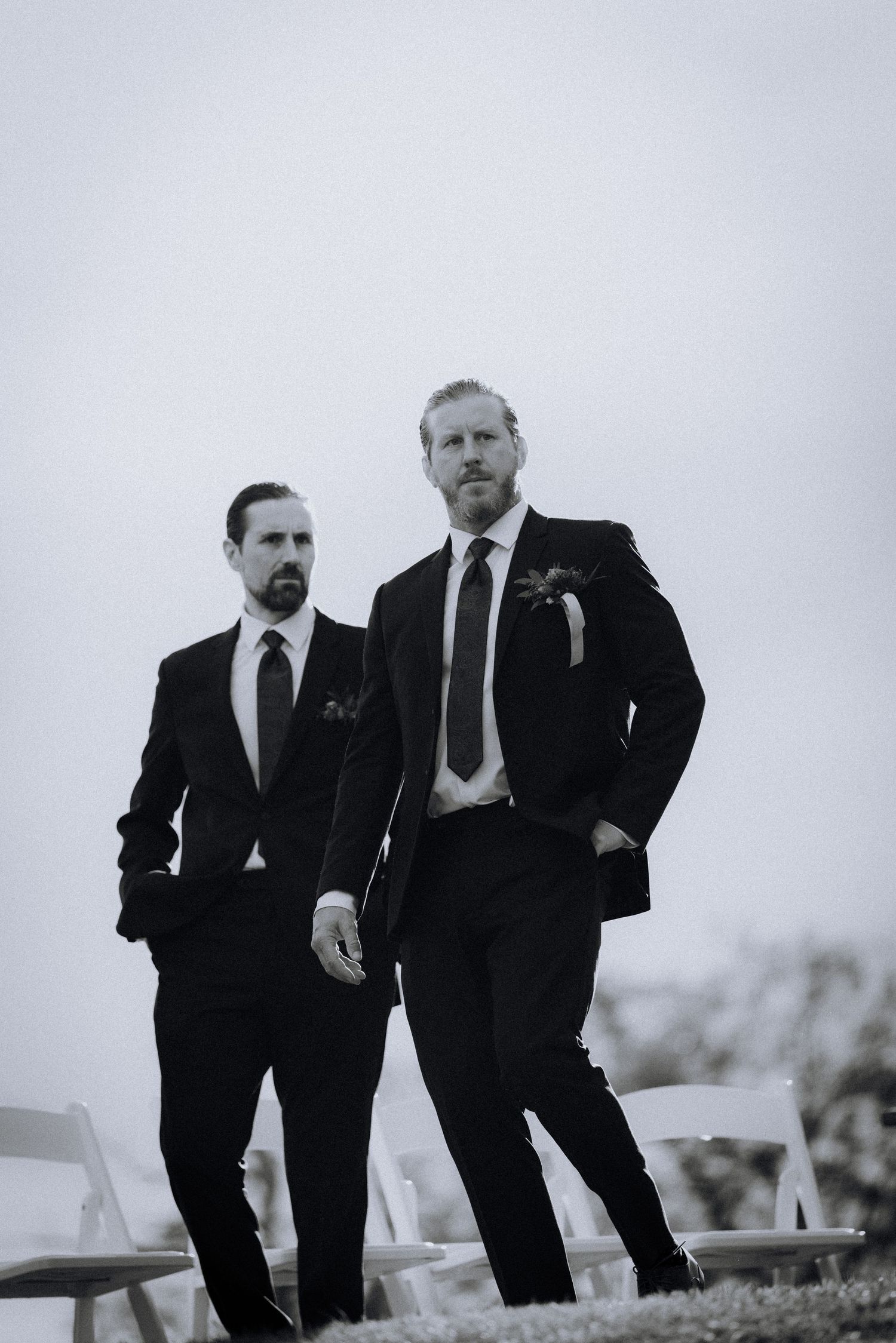 Two men in dark suits standing against an overcast sky in black and white.