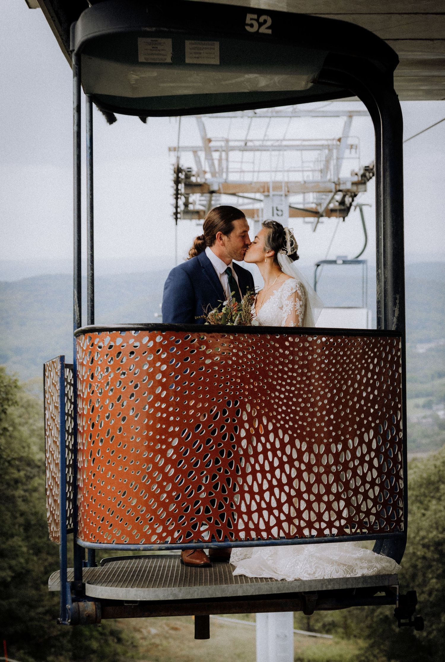 A couple shares a romantic moment on a ski lift chair with decorative metal details and mountain views in the background.