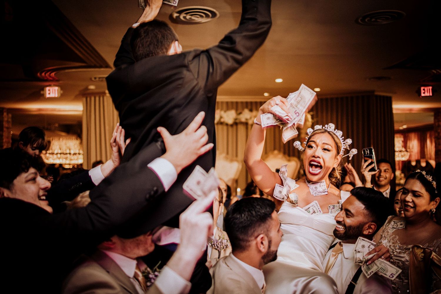 Joyful wedding celebration with guests lifting the bride and groom during traditional Jewish hora dance at reception.