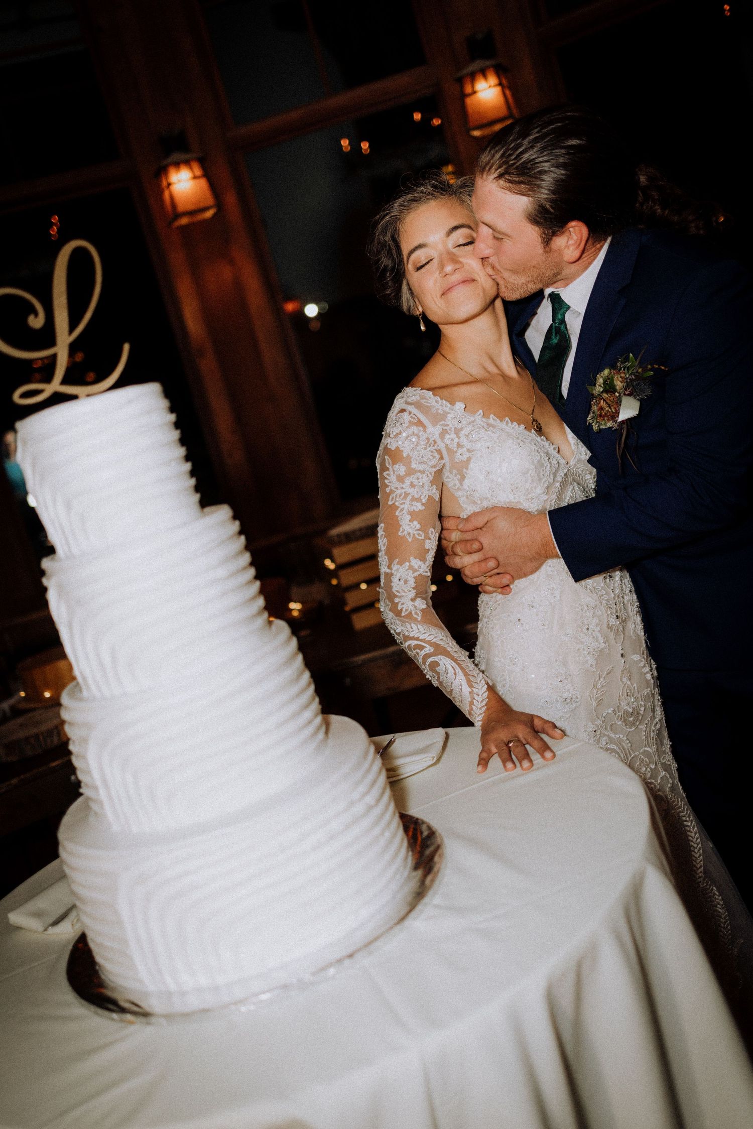 A wedding couple cuts into their elegant white tiered cake at their reception.