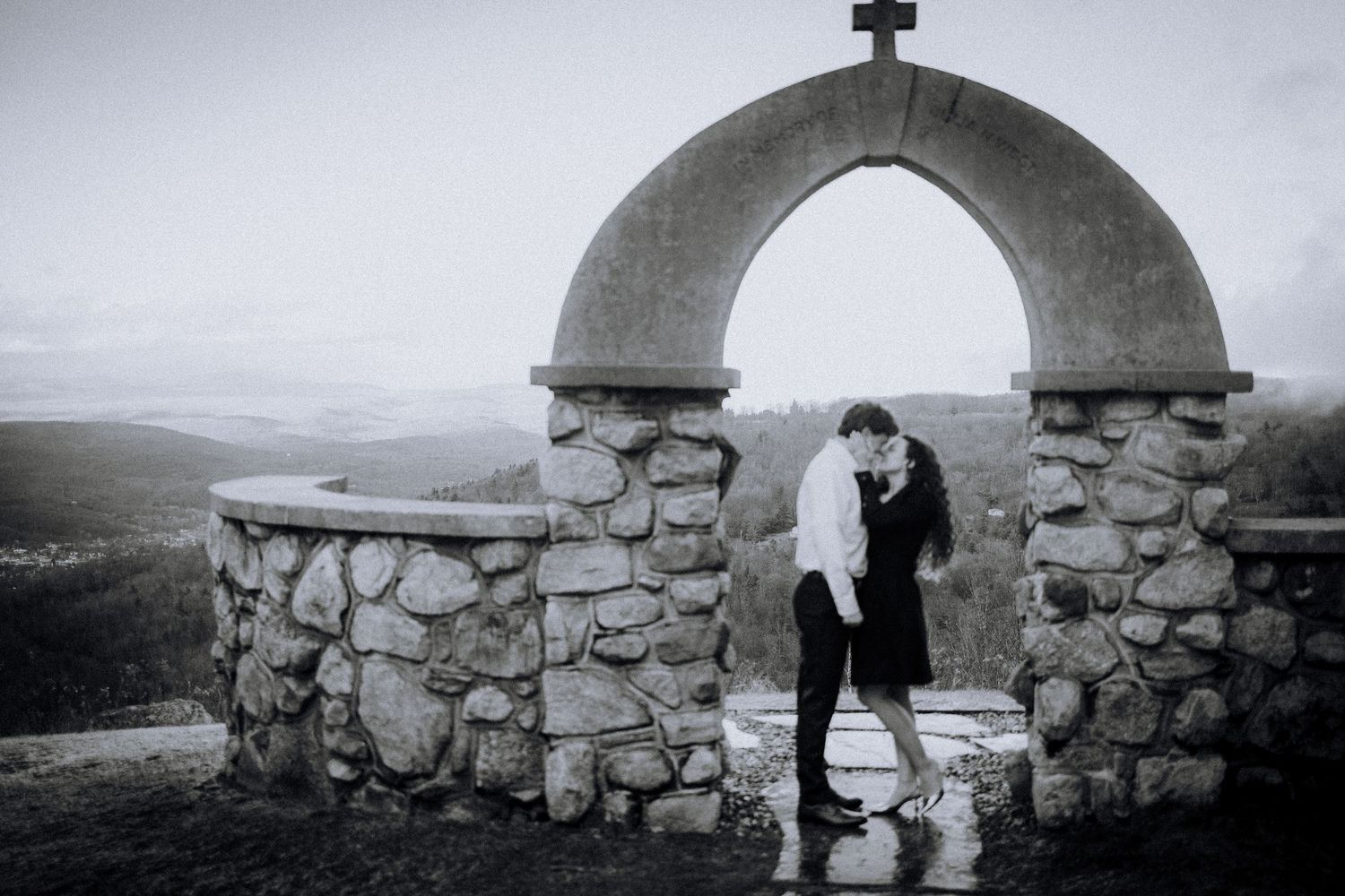 A couple embraces under a stone archway overlooking a misty landscape.