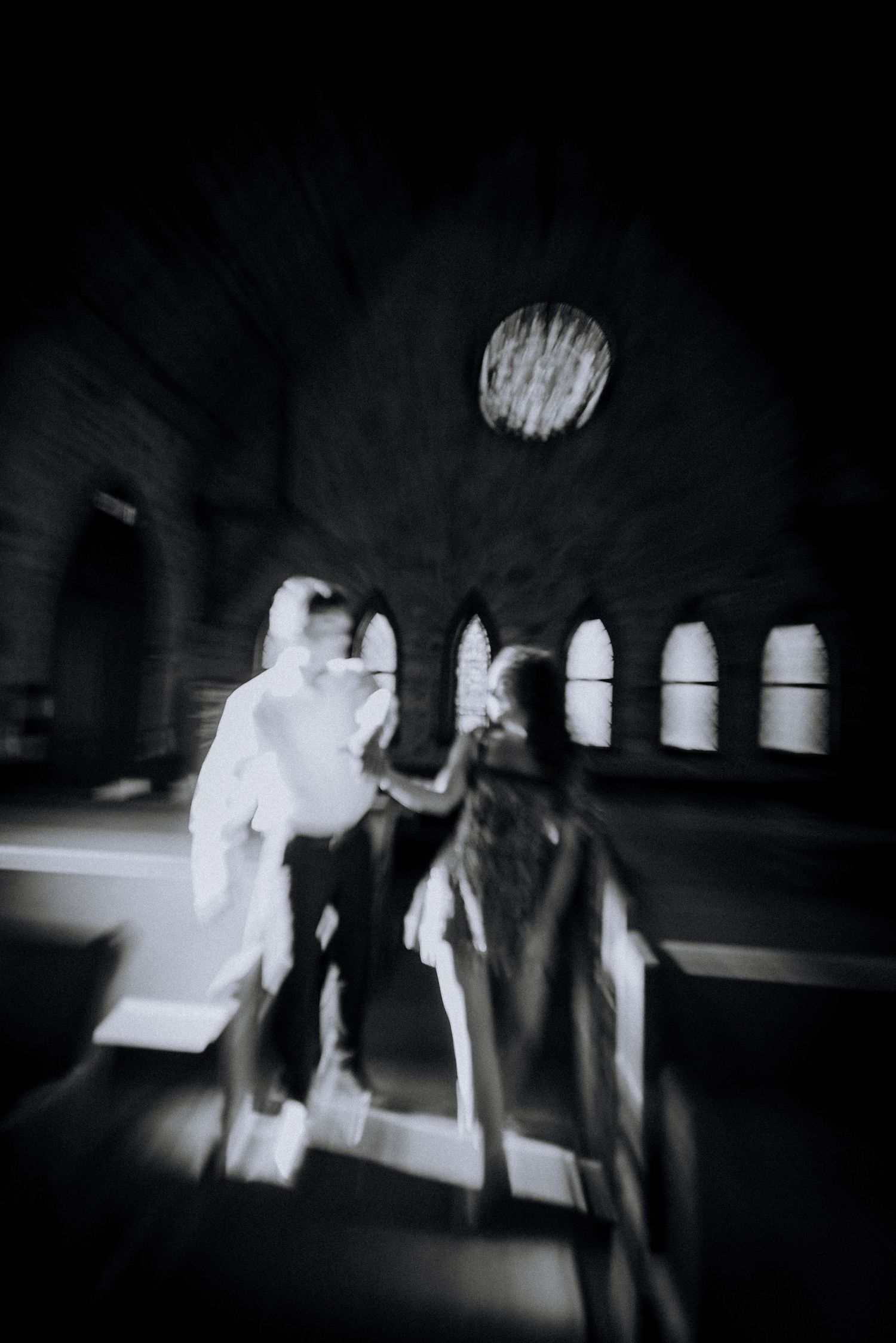 Blurred black and white motion photograph of people moving in a dark space.