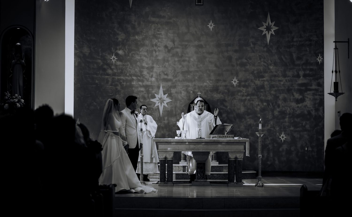 A black and white photo of a wedding ceremony at an altar with decorative stars on the wall.