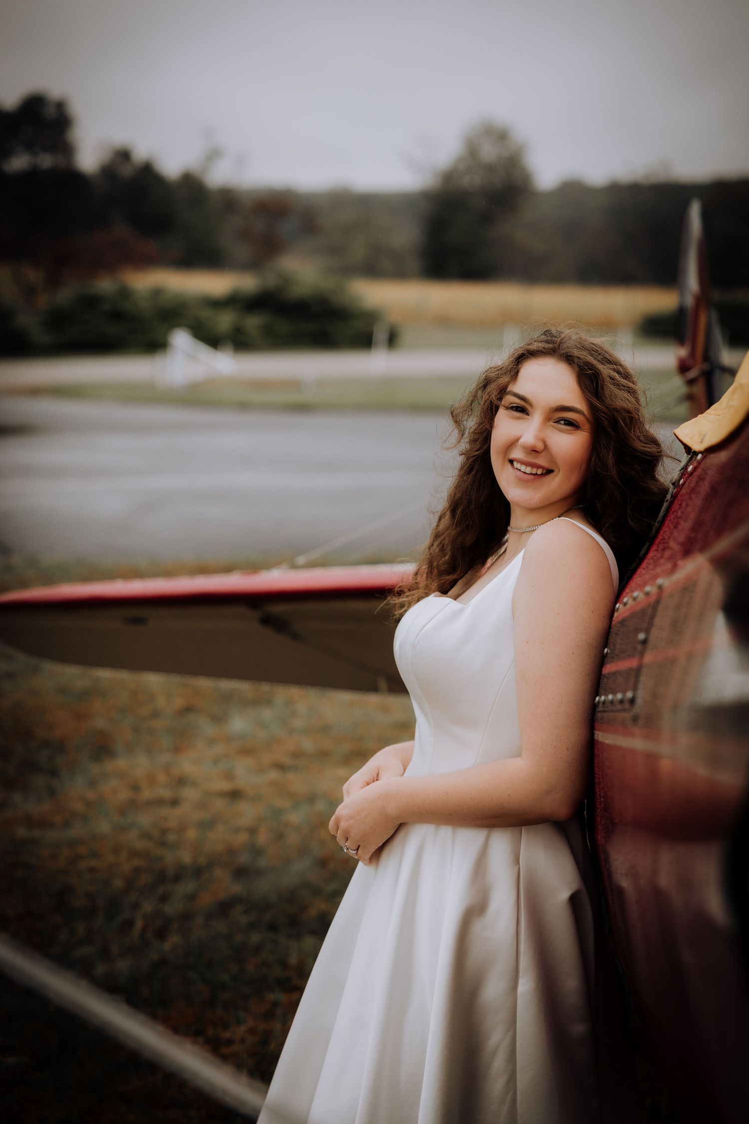 Bride poses against vintage red airplane during outdoor wedding photoshoot.
