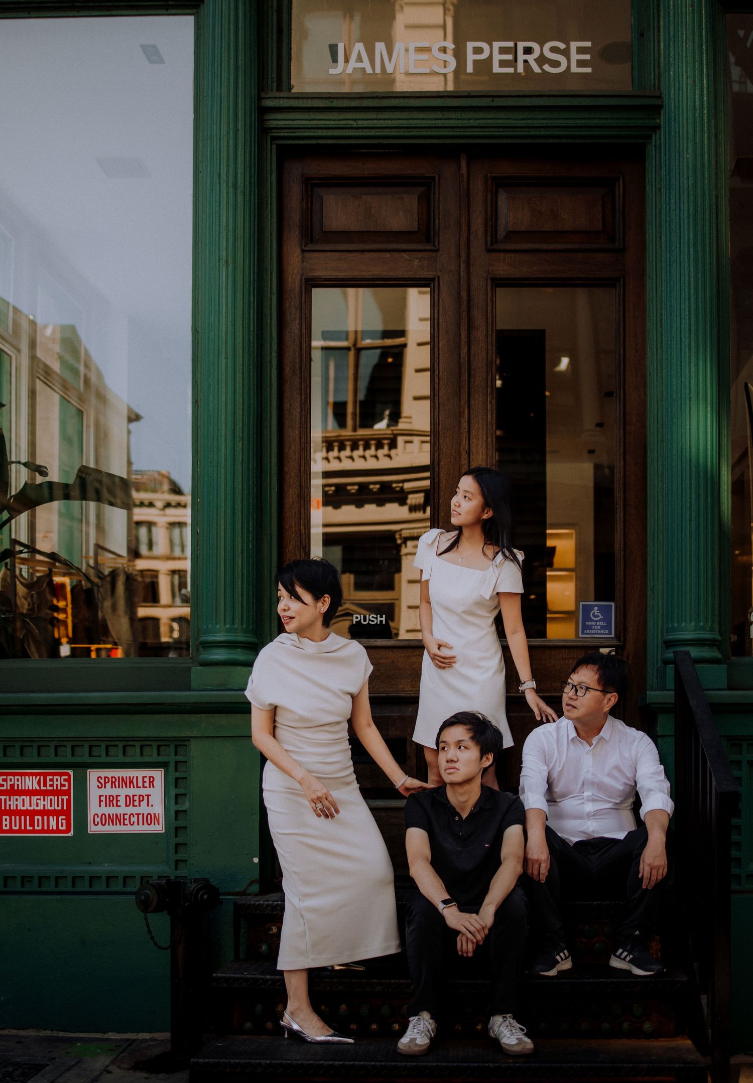 People in white outfits sitting and interacting outside a storefront with green columns.