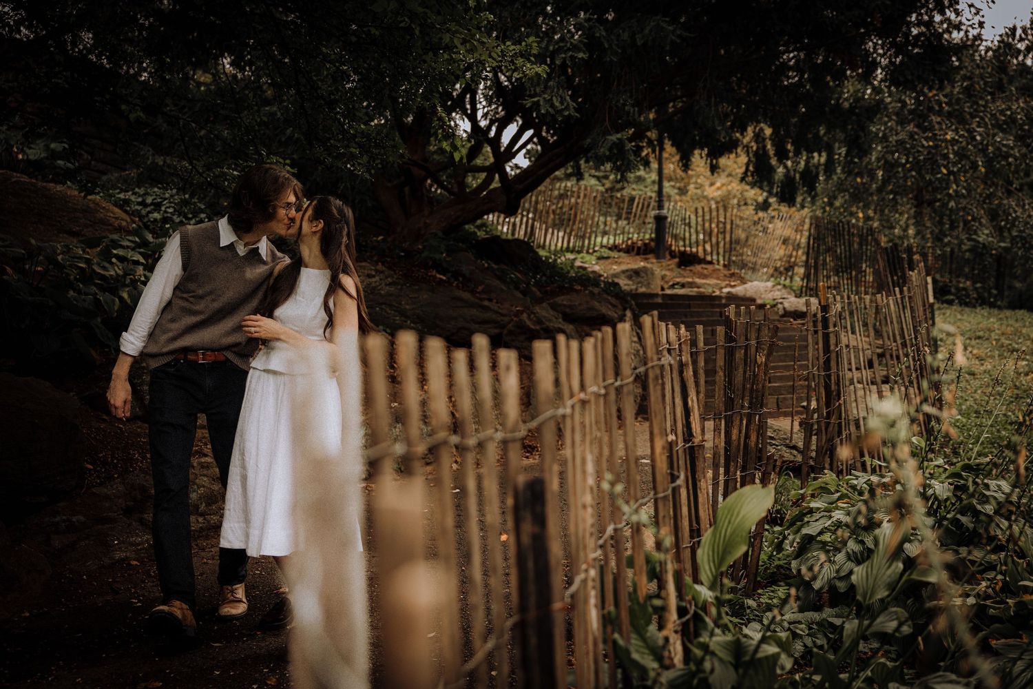 Couple walking along a weathered wooden fence in warm afternoon light.