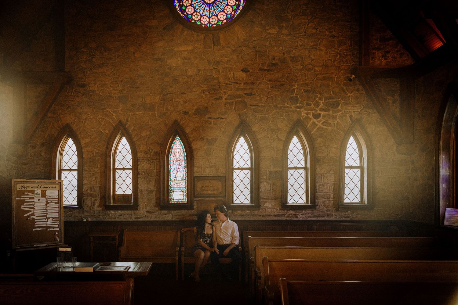 Historic stone church interior with arched windows and wooden pews bathed in natural light.