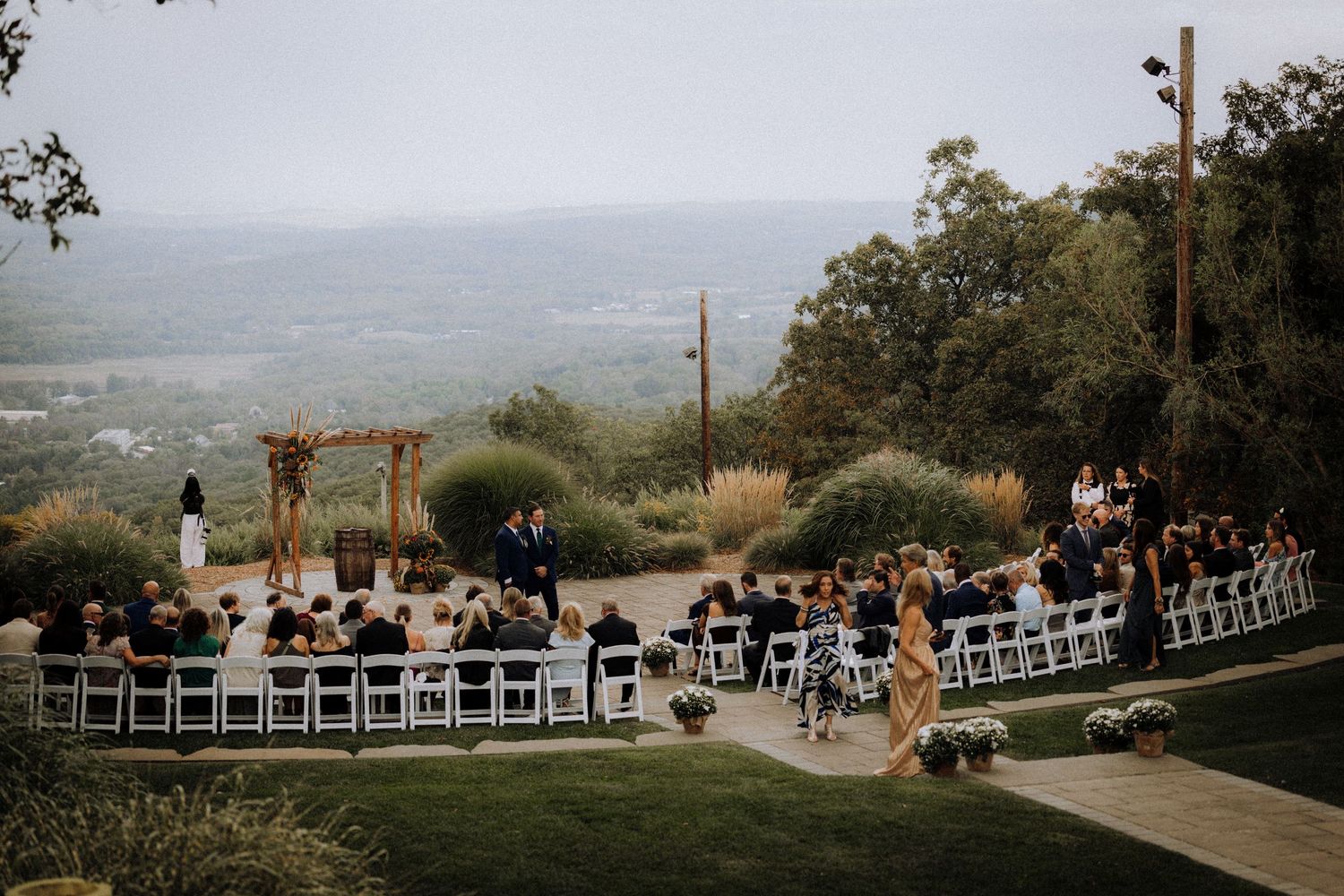 Outdoor wedding ceremony setup on a hillside with mountain views and white chairs.