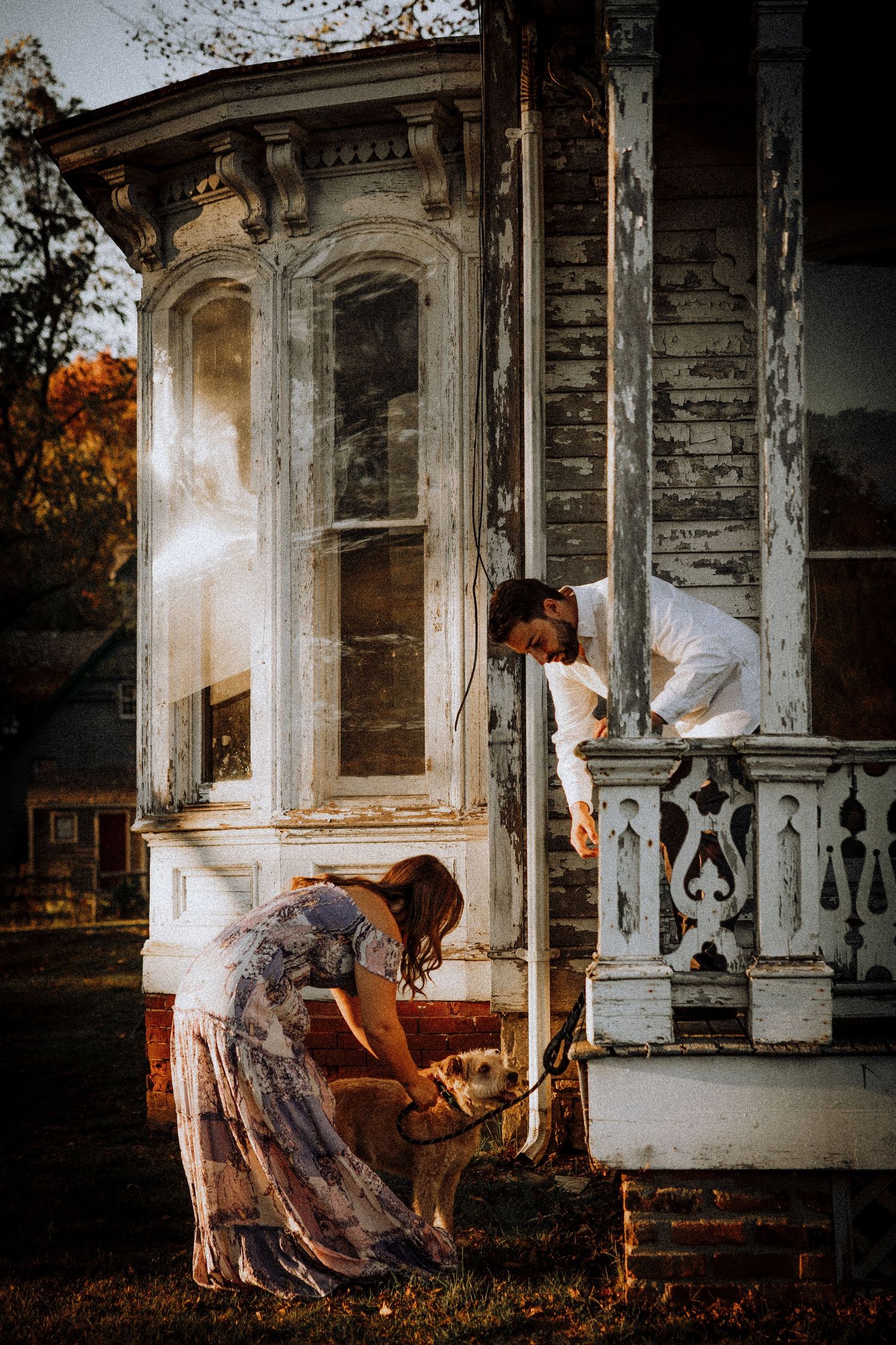 A couple explores the exterior of an old Victorian mansion during autumn.