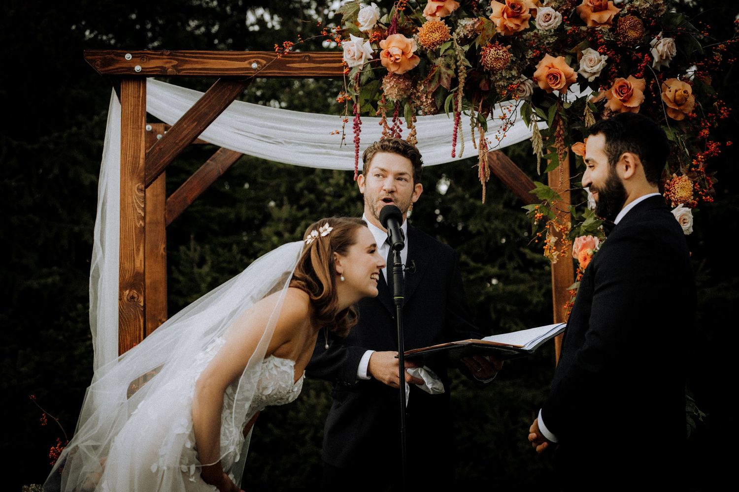 Romantic outdoor wedding ceremony setup with peach floral arrangements and white draping.