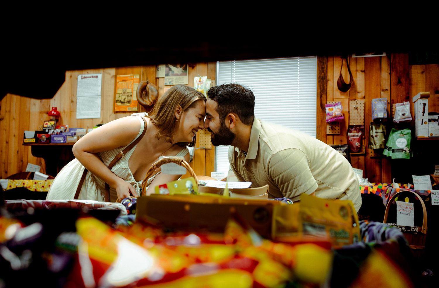 A couple shares an intimate moment while leaning over a restaurant counter filled with colorful snacks and candy.