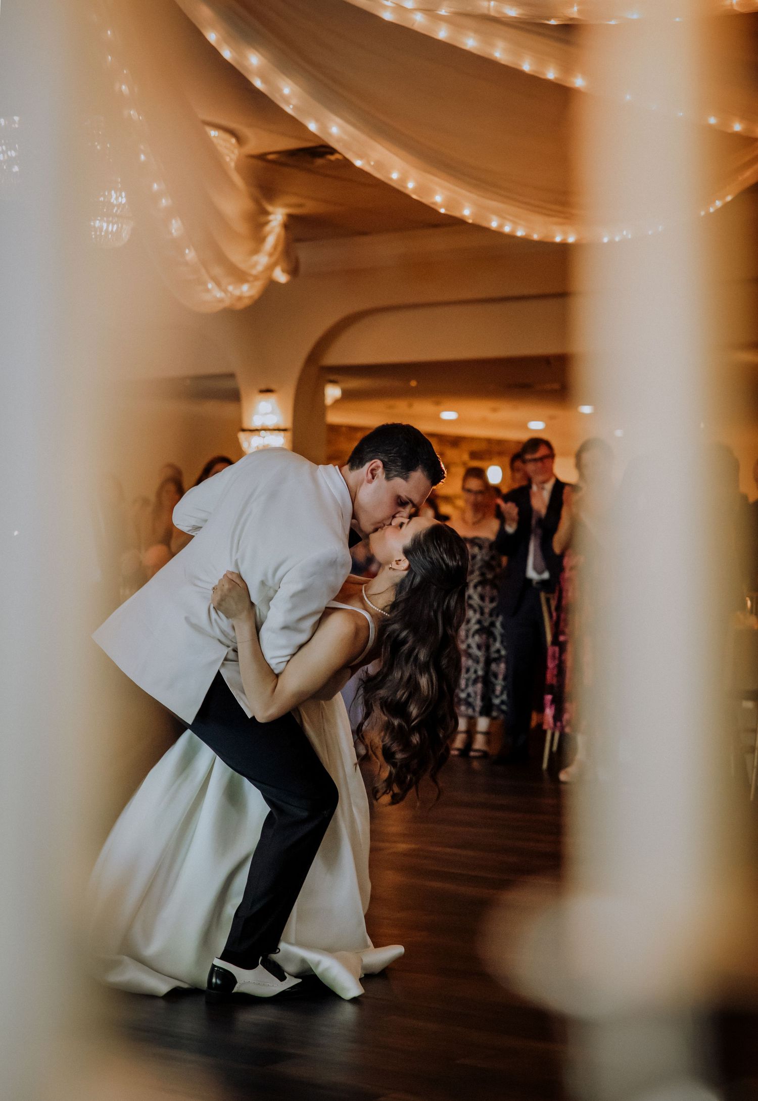 Dramatic dance move during a wedding reception under string lights and white pillars.